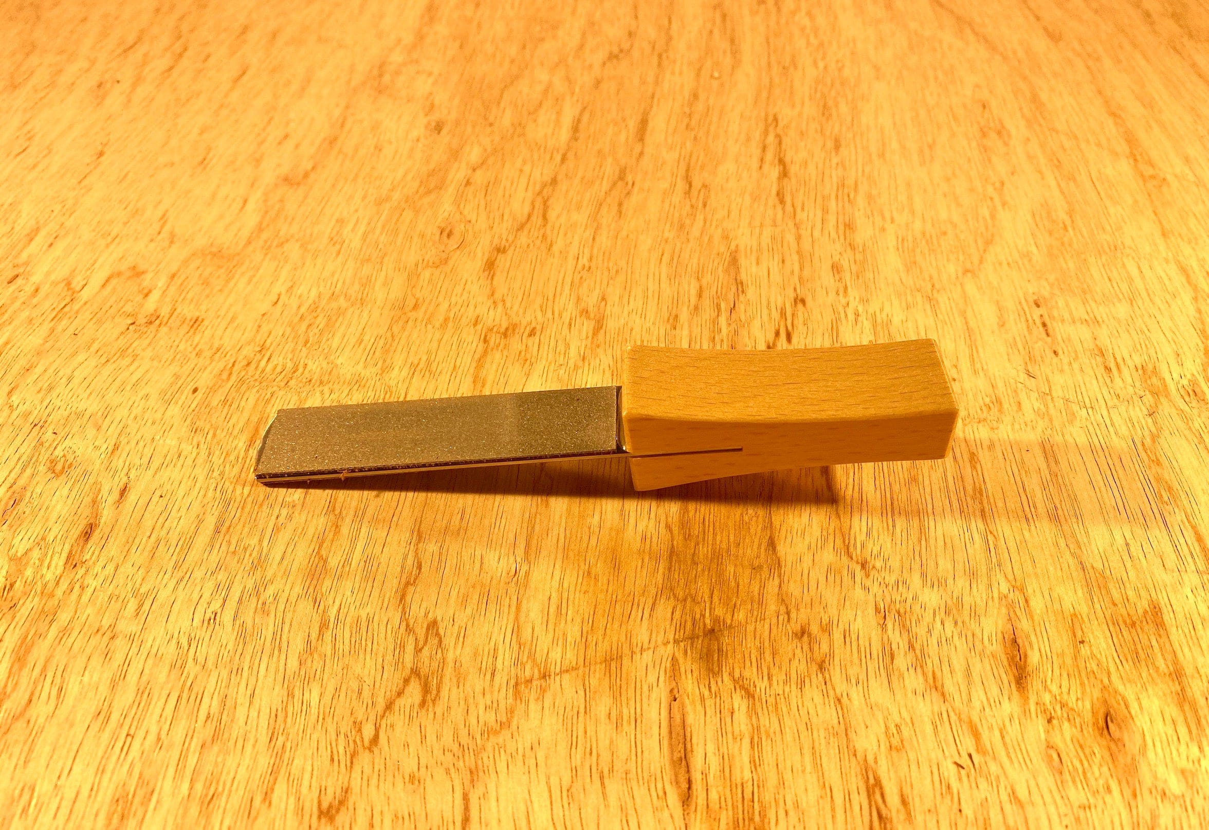 A Gransfors Bruk Sharpening Diamond File from GRF, featuring a sturdy wooden handle, lies flat on a wooden surface.