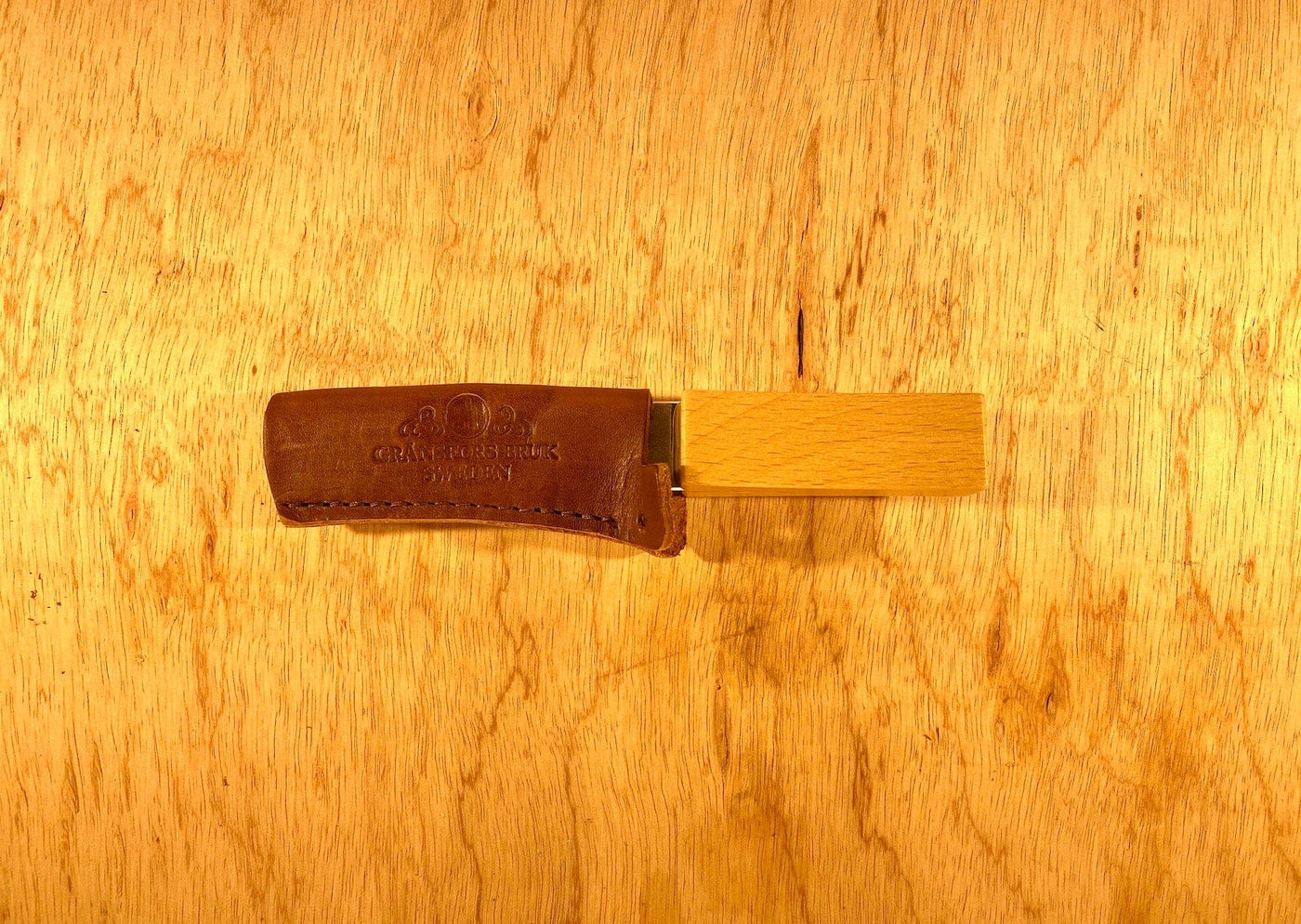 A Gransfors Bruk Sharpening Diamond File by GRF, featuring a wooden handle and a leather cover, rests on a wooden surface. This file is perfect for achieving both coarse and finer grit finishes.