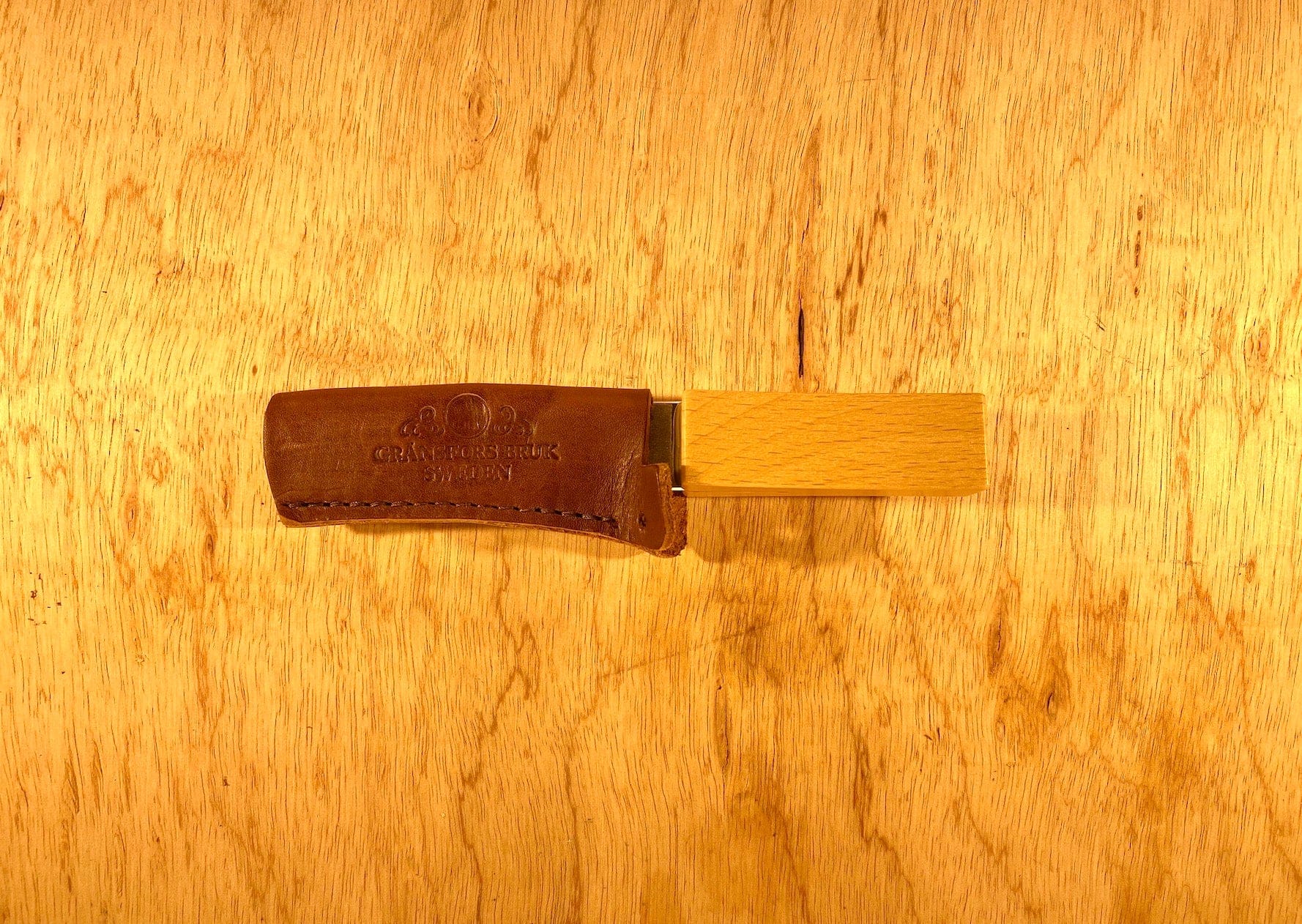 A Gransfors Bruk Sharpening Diamond File by GRF, featuring a wooden handle and a leather cover, rests on a wooden surface. This file is perfect for achieving both coarse and finer grit finishes.