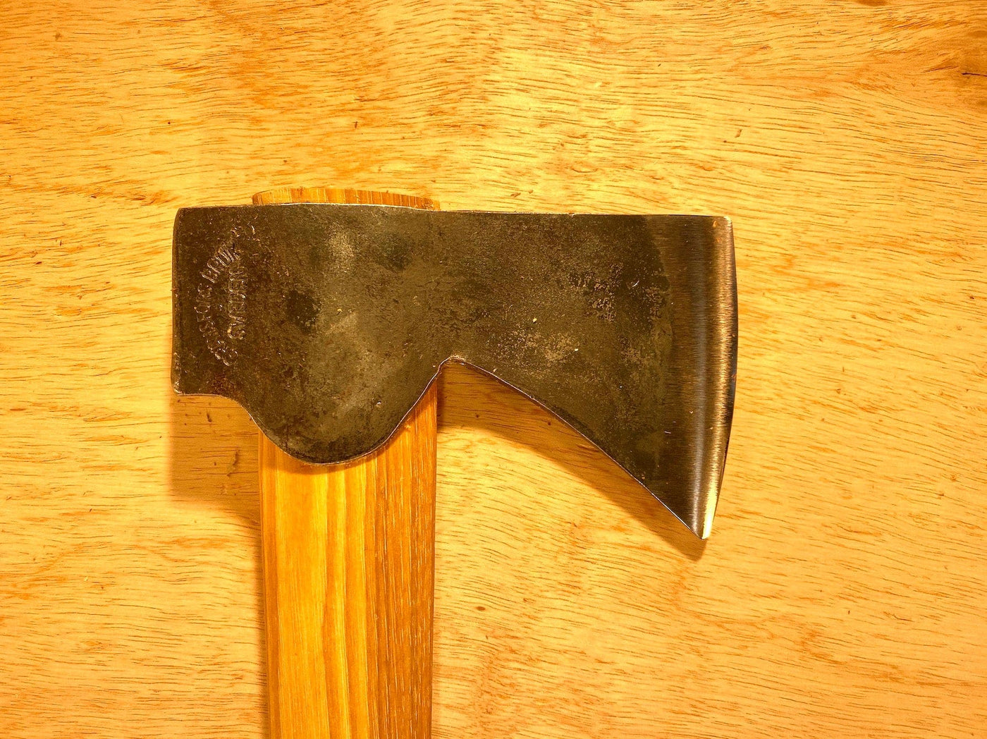A close-up of a GRF Gransfors Bruk Wildlife Hatchet with a wooden handle on a wooden surface. This expertly crafted tool reflects traditional craftsmanship, perfect for outdoor adventures.