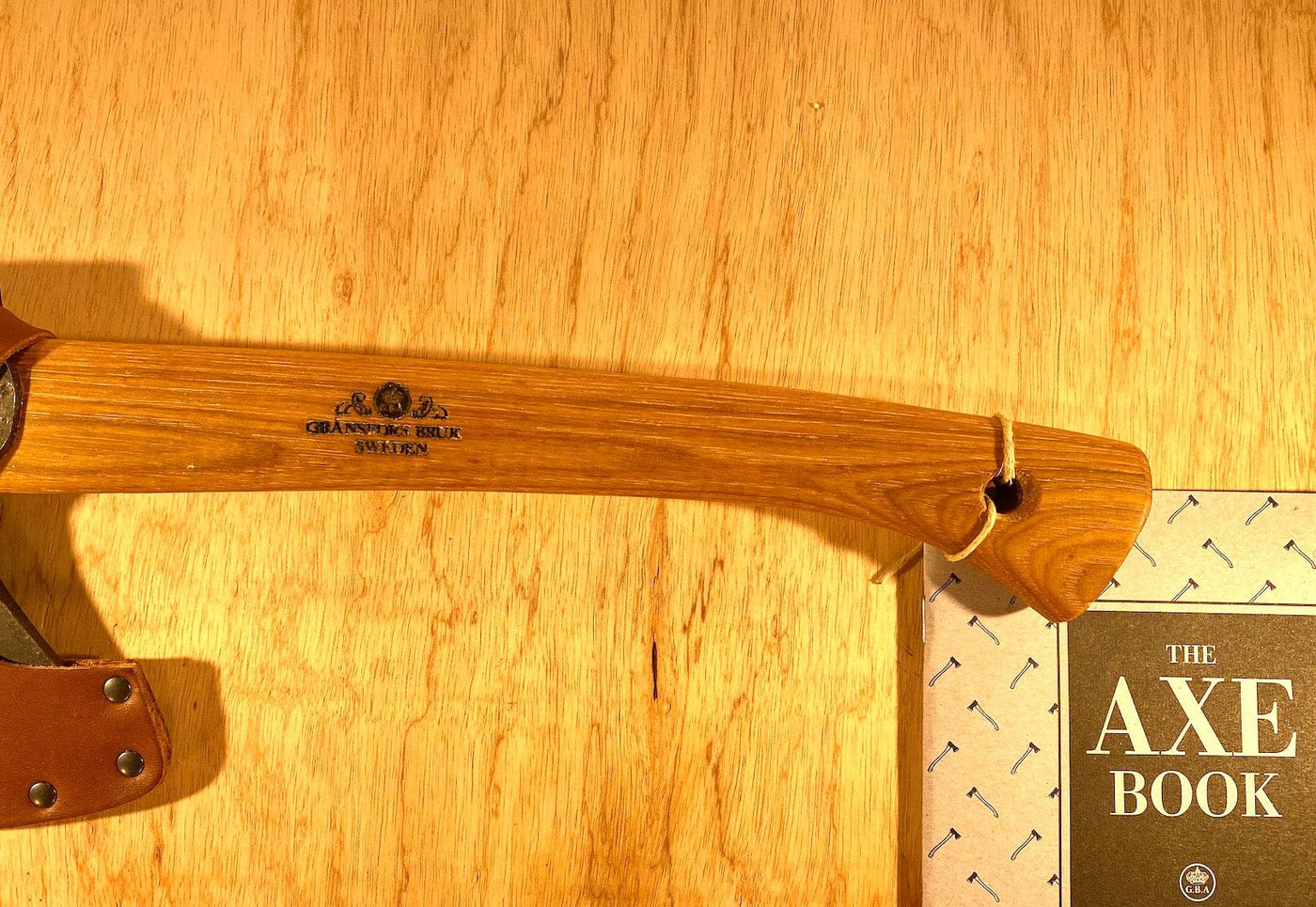 The GRF Gransfors Bruk Wildlife Hatchet handle elegantly rests on "The Axe Book" against a rustic wooden background, capturing the essence of traditional craftsmanship for outdoor adventures.
