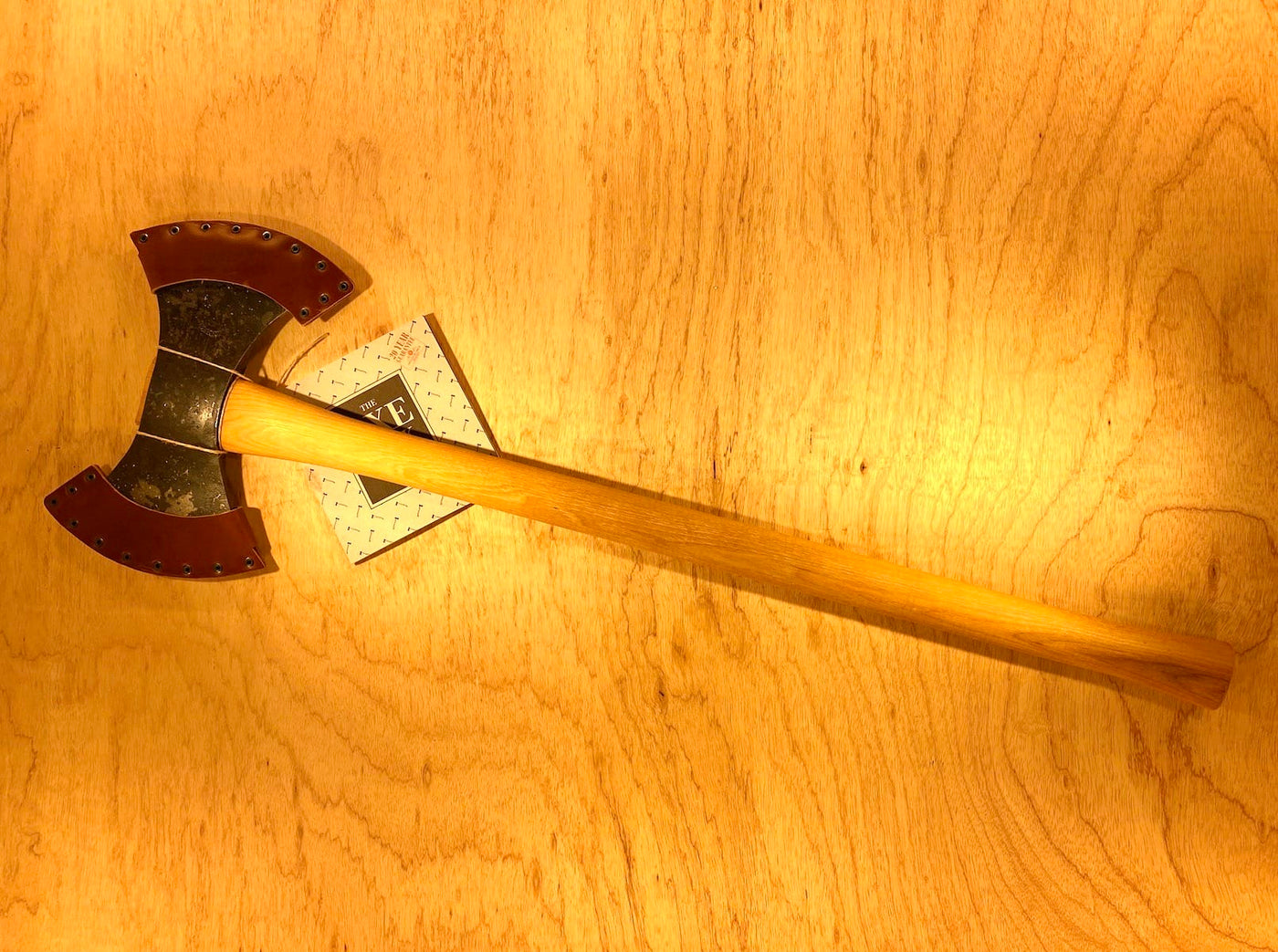 A GRF Gransfors Bruk Double Bit Axe 35in Handle, featuring sharp metal blades and a wooden handle, lies on a light wood surface, perfect for axe throwing enthusiasts.