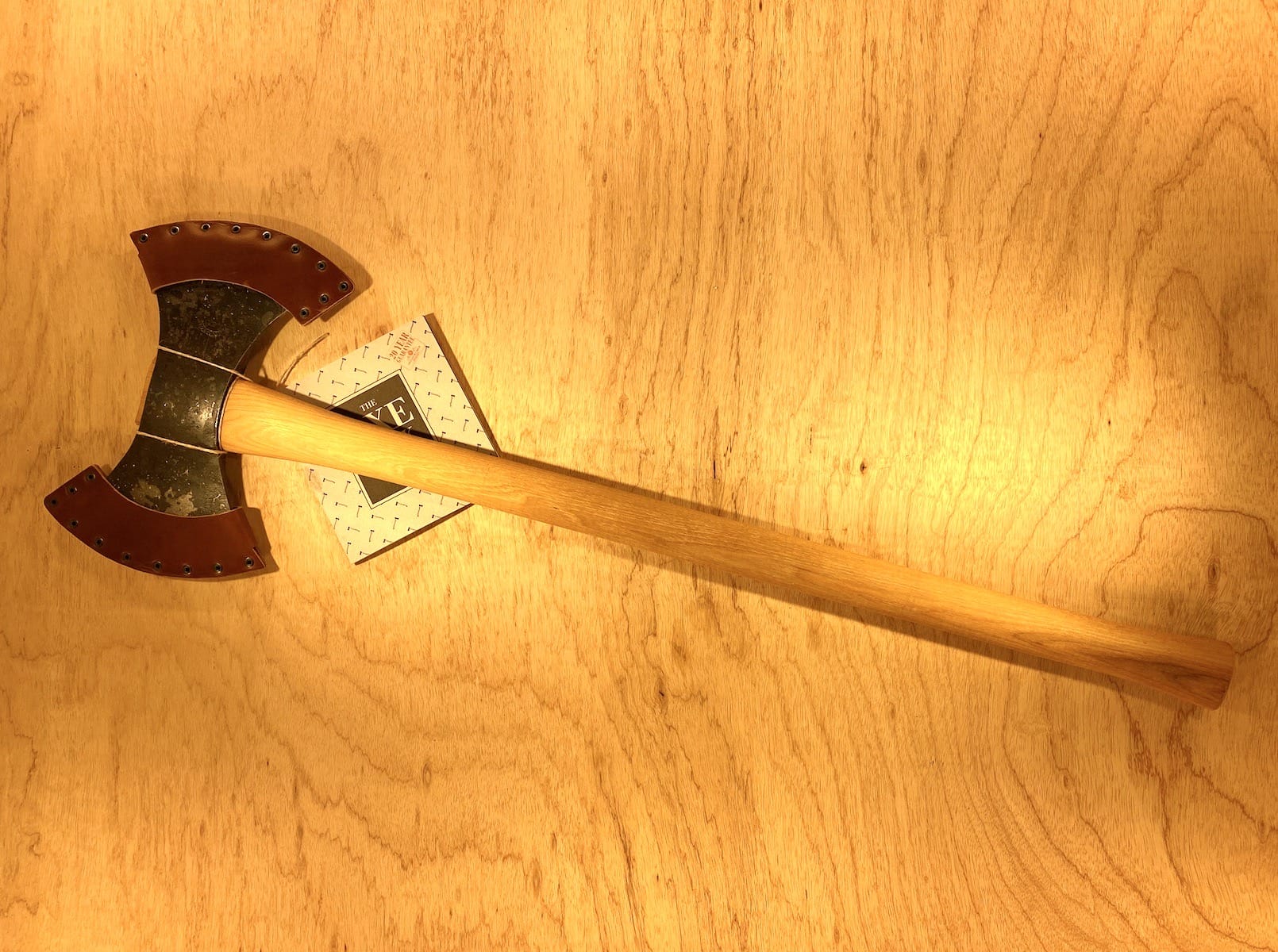 A GRF Gransfors Bruk Double Bit Axe 35in Handle, featuring sharp metal blades and a wooden handle, lies on a light wood surface, perfect for axe throwing enthusiasts.