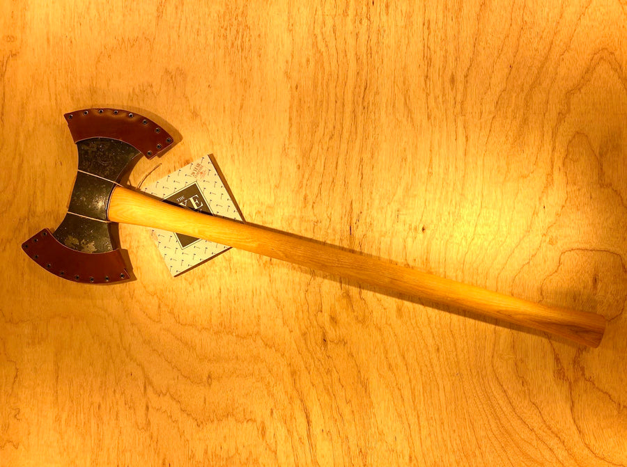 A GRF Gransfors Bruk Double Bit Axe 35in Handle, featuring sharp metal blades and a wooden handle, lies on a light wood surface, perfect for axe throwing enthusiasts.