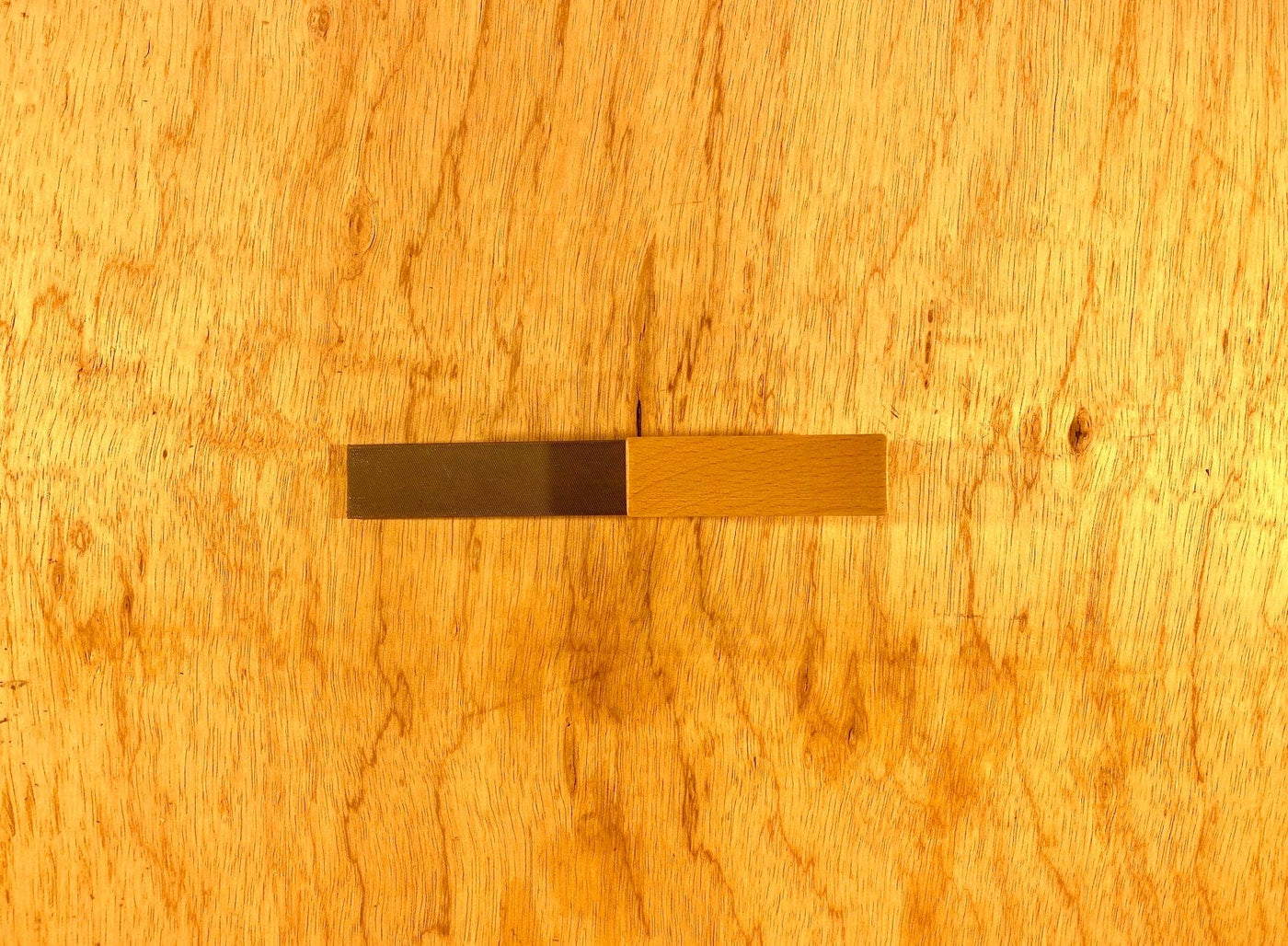 Two small rectangular swatches, one dark brown and one light brown, rest on a wooden surface, resembling the contrast of an aged leather sheath against the gleam of a Gransfors Bruk Axe File by GRF.