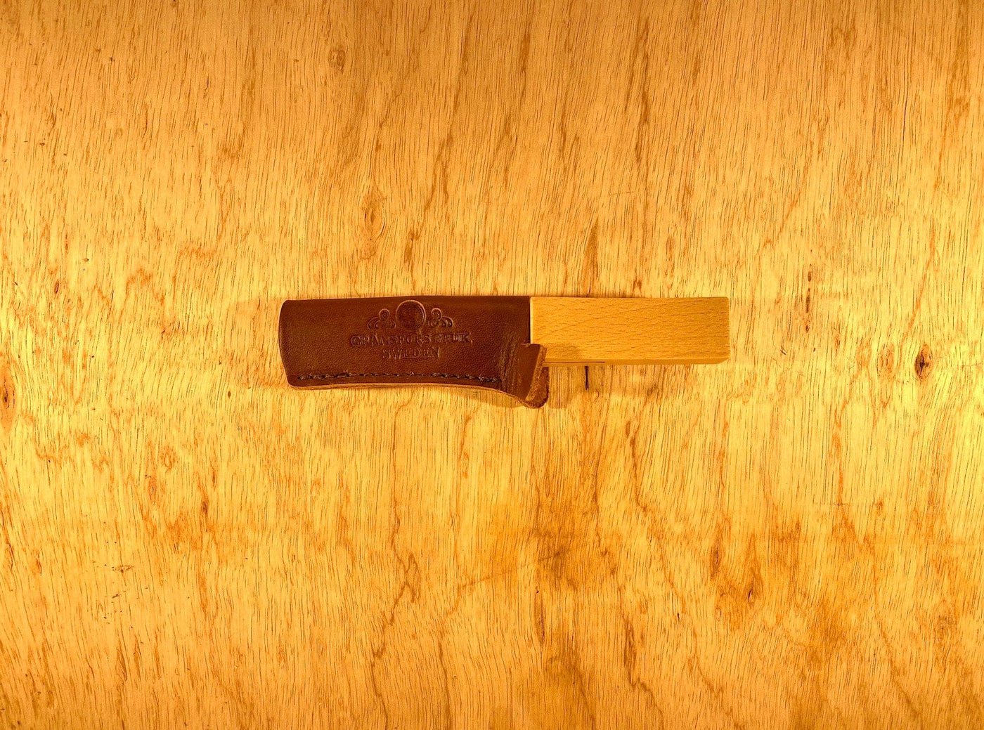 A Gransfors Bruk Axe File from GRF, housed in a brown leather sheath, lies on a light wood surface.