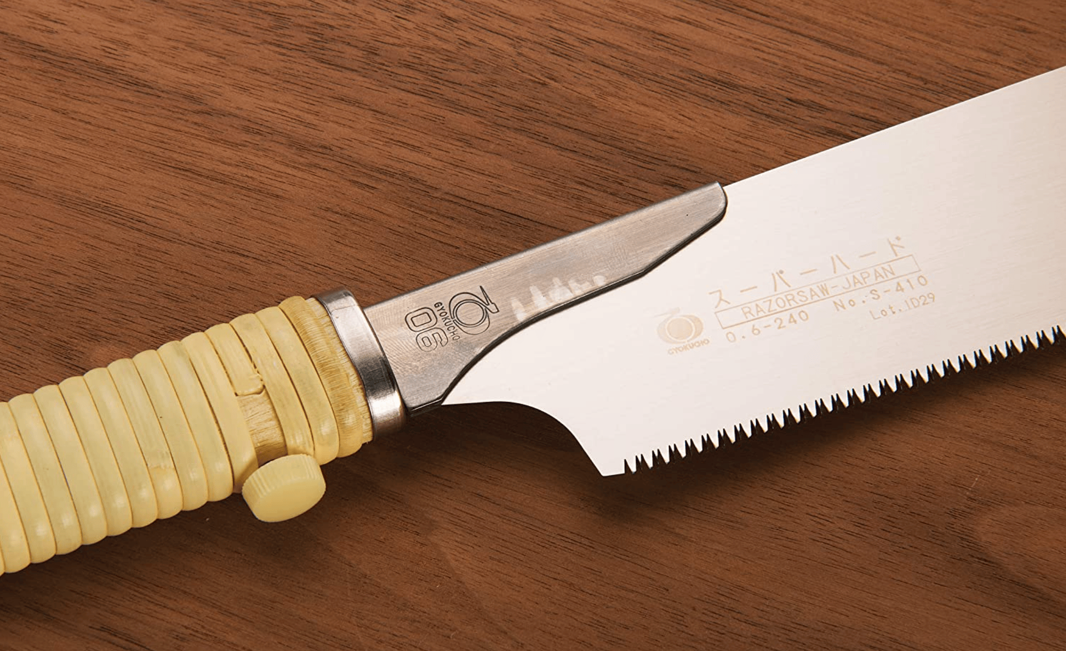 Close-up of a BBT Gyokucho Crosscut Razorsaw 240mm with a yellow ribbed handle and toothed metal blade, ideal for precision cutting, resting on a wooden surface.