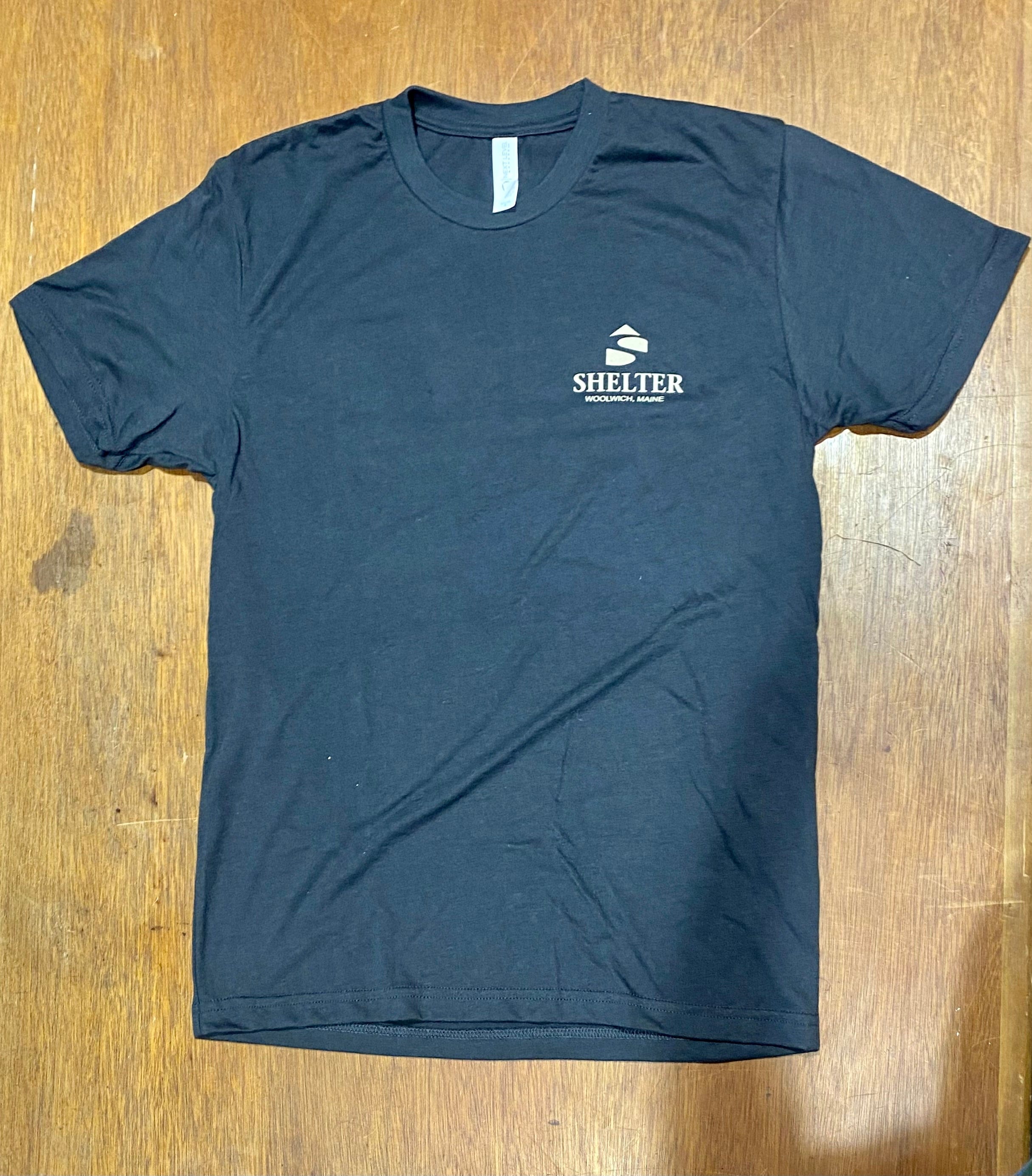 HighPine's "That is one Slick T-Shirt," featuring "Shelter" and a logo on the left chest, elegantly placed on a wooden surface.