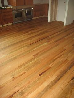A kitchen with wooden cabinets made from reclaimed wood, two built-in ovens, and a hardwood floor finished with HNF's Heritage Natural Finishes Concentrate.