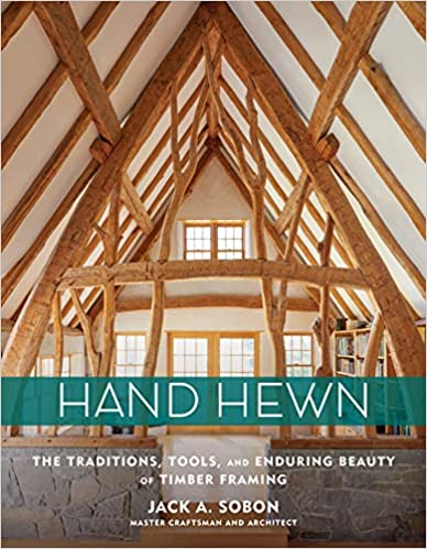 Cover of "Hand Hewn: The Traditions, Tools, and Enduring Beauty of Timber Framing" by Ingram Content Group shows a timber-framed interior with exposed beams and windows, highlighting traditional building methods.