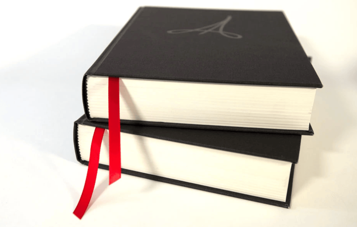 Two thick, black hardcover books sit stacked on a plain white background, each with a red ribbon bookmark. The top book is The Anarchists Design Book: Expanded Edition by LAP, evoking themes of woodworking and furniture design.
