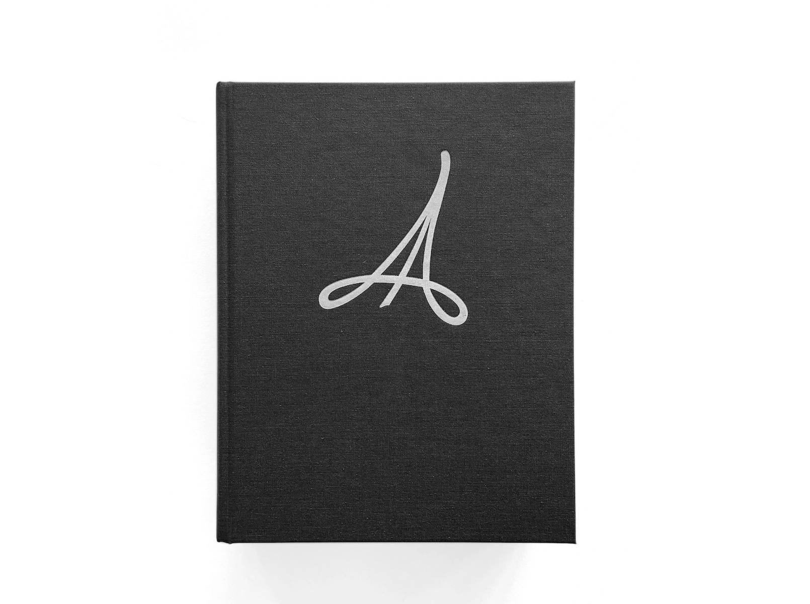 A black hardcover The Anarchists Design Book: Expanded Edition by LAP features a large, elegant silver cursive A centered on the front—an homage to its modern influence in furniture design and woodworking. Photographed on white.