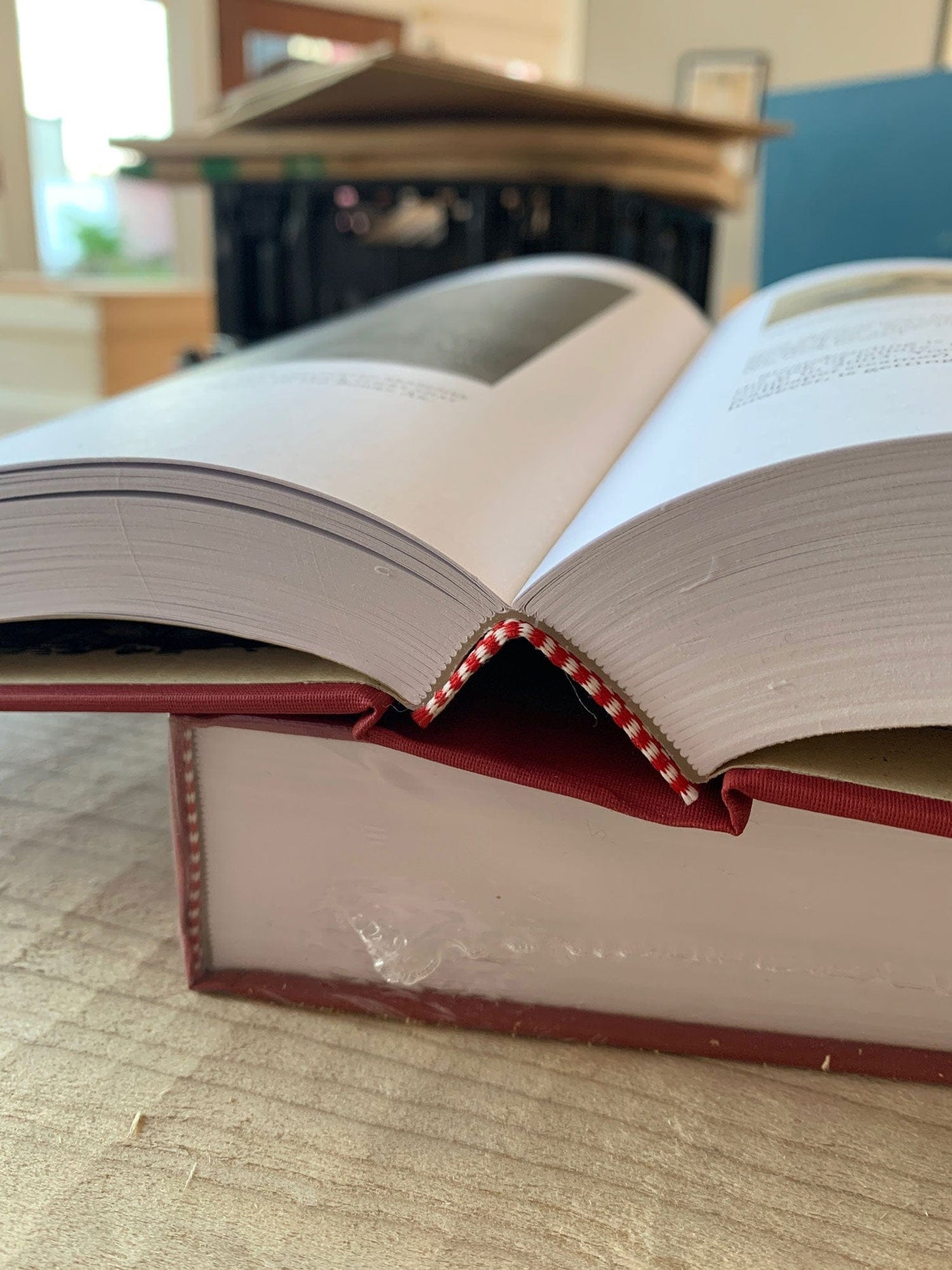 An open copy of "The Stick Chair Book" by LAP rests on a closed one, showcasing its spine and pages. In the blurred background, vernacular furniture subtly enhances the scene, with woodworking tools adding character to the desk scattered with other books.