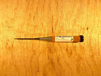 A professional-grade Fujikawa Oire Bench Chisel by MARU with a wooden handle and metal blade rests on the wooden surface. A label with text adorns the handle, showcasing its craftsmanship. Ideal for precision work, this tool embodies the artistry of Japanese chisels crafted from white steel laminated for durability.