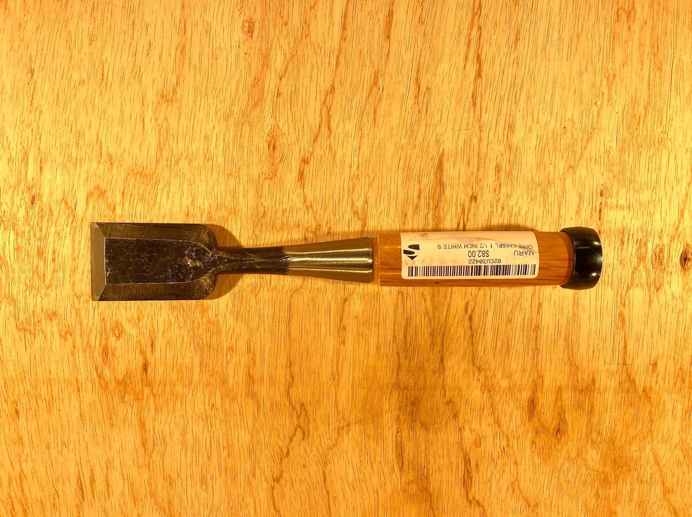 A MARU Fujikawa Oire Bench Chisel with a wooden handle rests on a wooden surface, featuring a blade crafted from white steel laminated for superior performance.