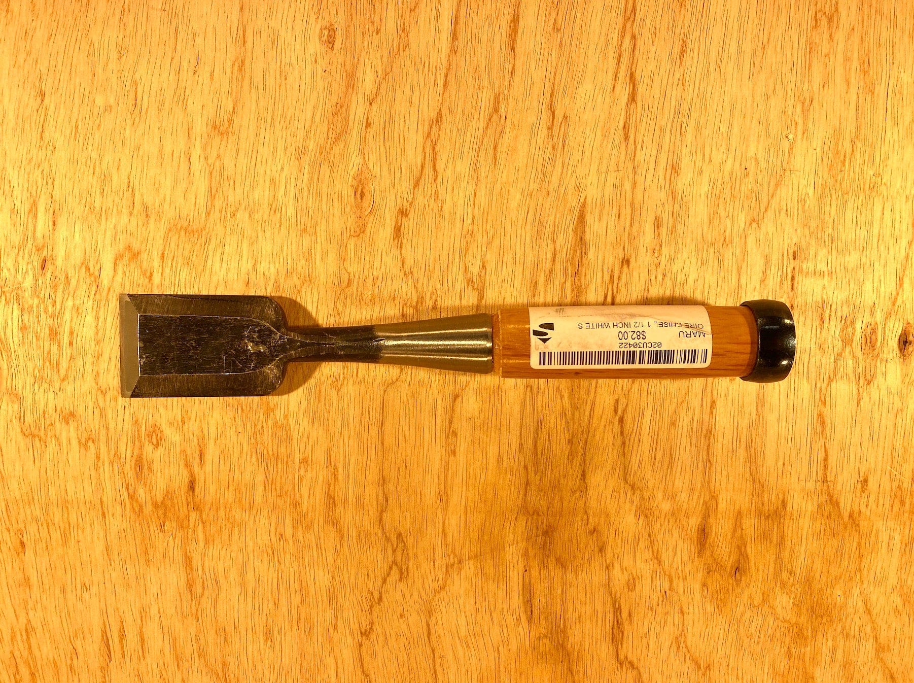 A MARU Fujikawa Oire Bench Chisel with a wooden handle rests on a wooden surface, featuring a blade crafted from white steel laminated for superior performance.