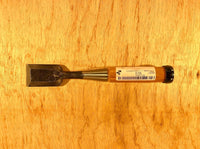 A MARU Fujikawa Oire Bench Chisel with a wooden handle rests on a wooden surface, featuring a blade crafted from white steel laminated for superior performance.