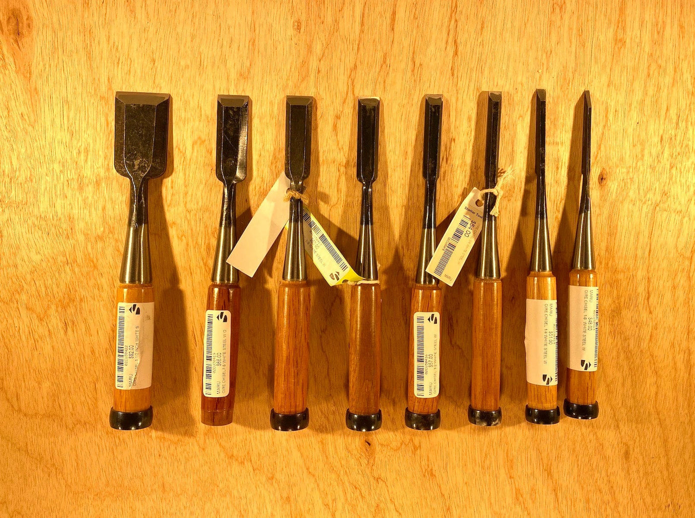 A set of Fujikawa Oire Bench Chisels by MARU, featuring professional-grade white steel laminated blades and wooden handles, elegantly arranged on a wooden surface.