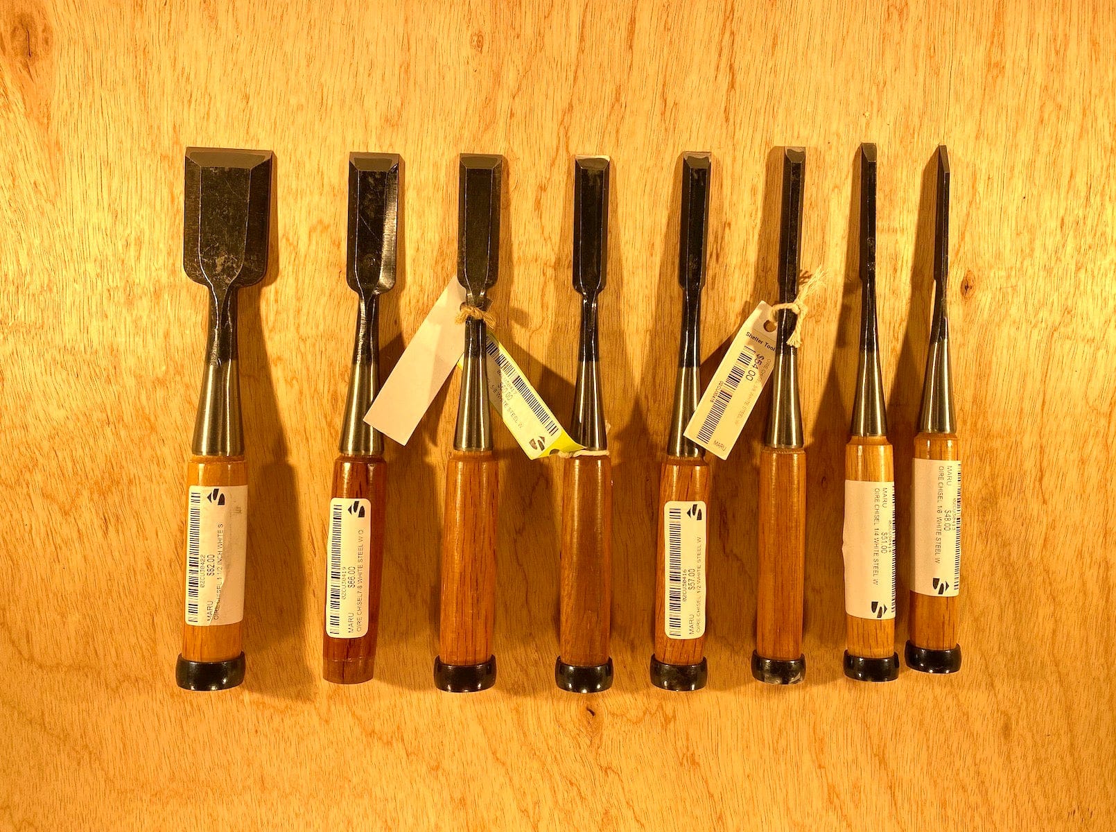 A set of Fujikawa Oire Bench Chisels by MARU, featuring professional-grade white steel laminated blades and wooden handles, elegantly arranged on a wooden surface.