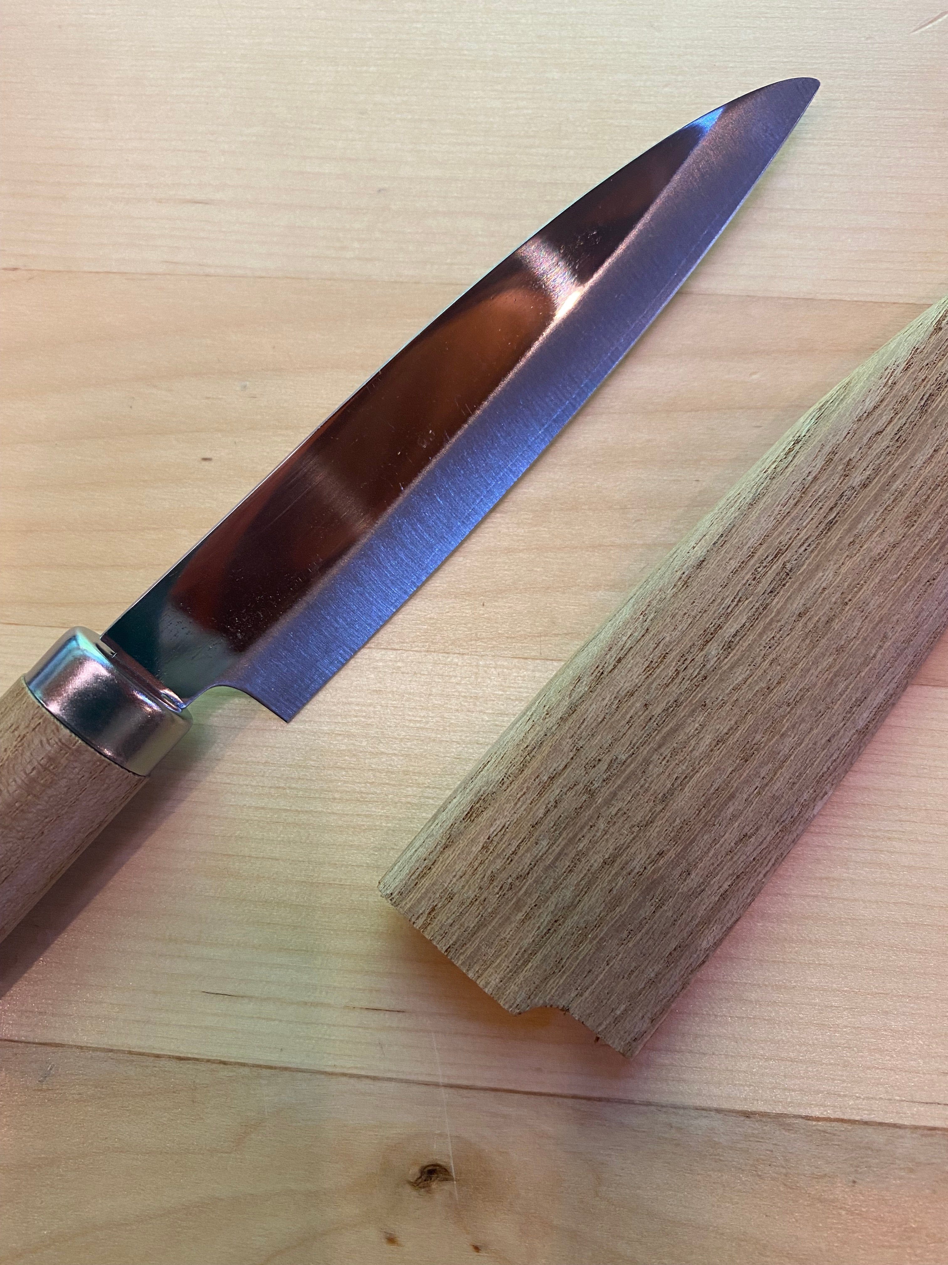 The MARU FRUIT KNIFE, featuring an oak handle and a polished stainless steel blade, is placed next to a wooden sheath on a light wooden surface.