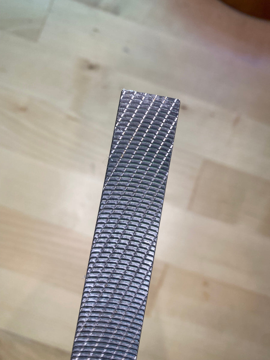 A close-up of an Iwasaki Wood File by MARU, featuring its textured, rectangular metal design with a grid pattern surface, is showcased on a light wooden floor. Celebrated for its innovative Japanese design, this tool offers rapid cutting action with precision and efficiency.