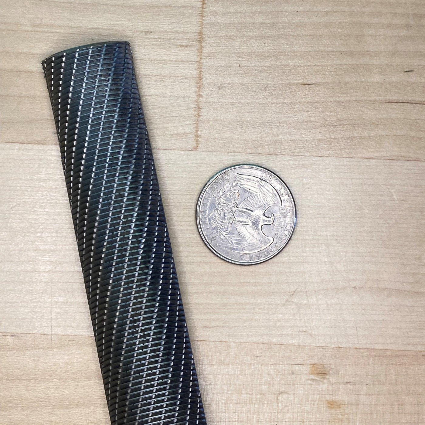 A textured black cylindrical object stands vertically beside a coin on a wooden surface, showcasing the precision and craftsmanship of innovative Japanese tools like the MARU Iwasaki Wood Files, renowned for their rapid cutting action.