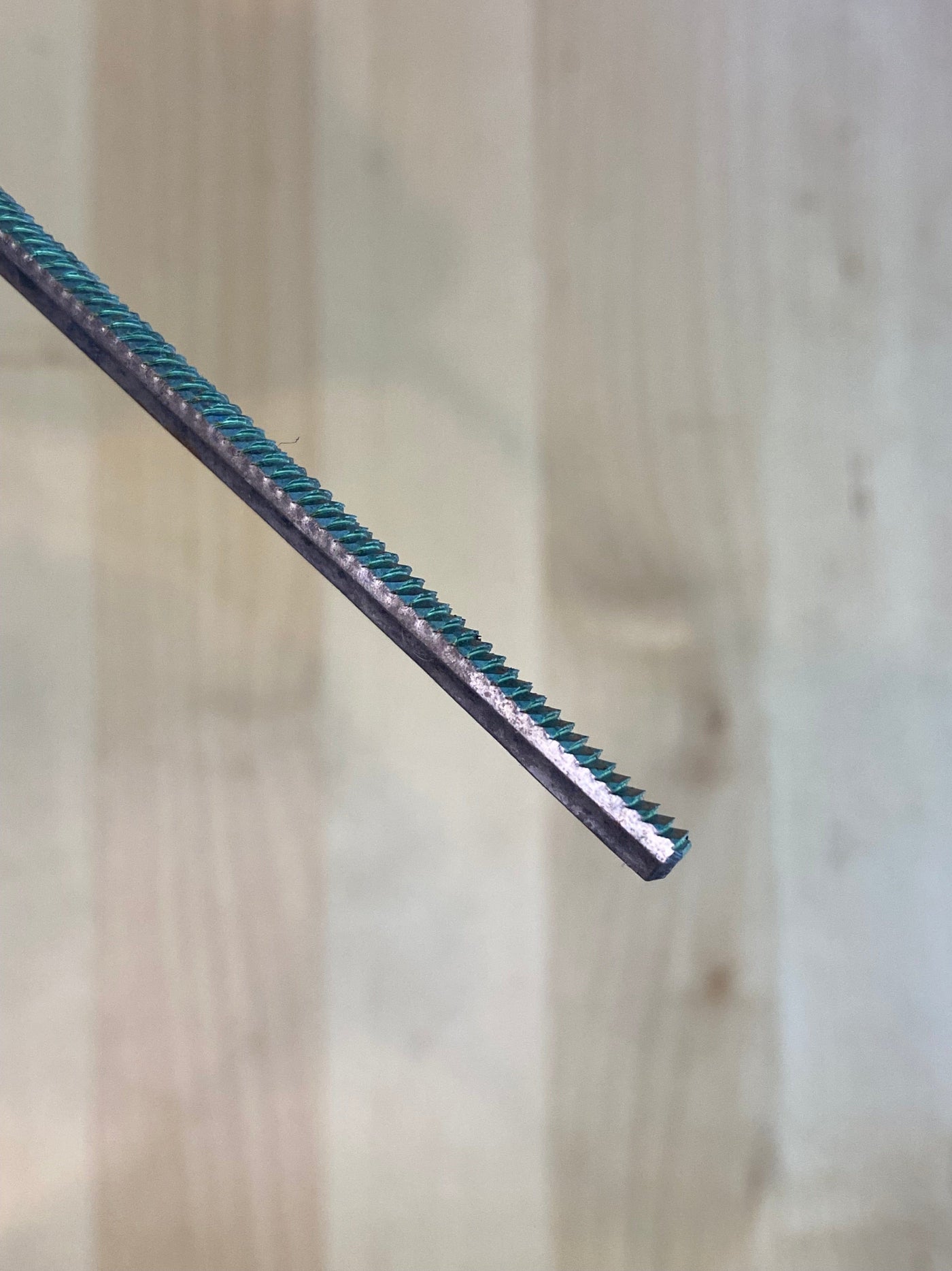 Diagonal close-up of a MARU Iwasaki Half Round Ex Fine W/Grip, featuring a turquoise and silver textured metal rod with ridged surface against a blurred wooden background; an essential tool in any woodworker's kit.
