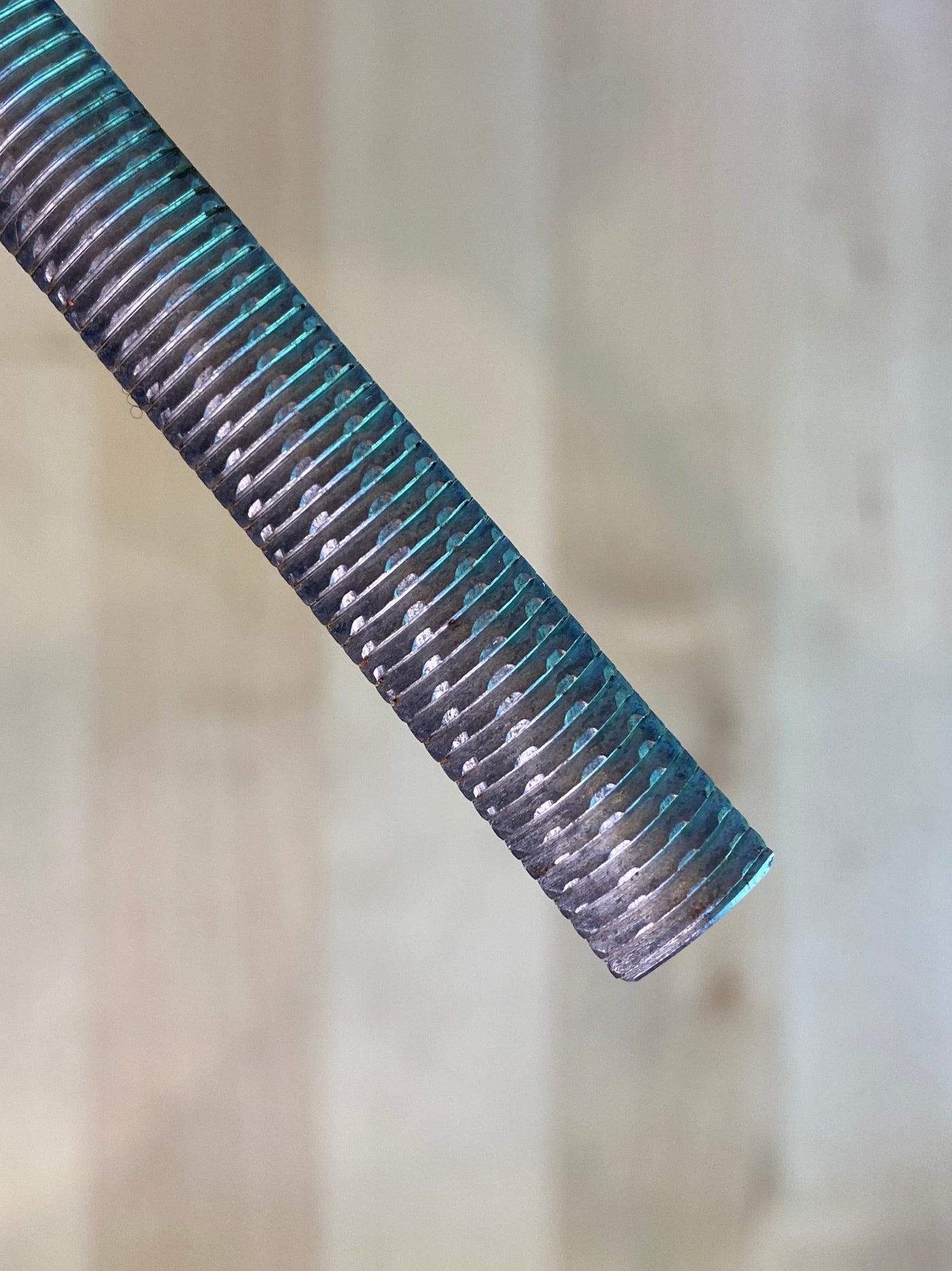 A close-up of a MARU Iwasaki Half Round Ex Fine W/Grip metal rod with horizontal grooves, positioned diagonally against a neutral background, highlights its role as a precision tool in a woodworker's toolkit.
