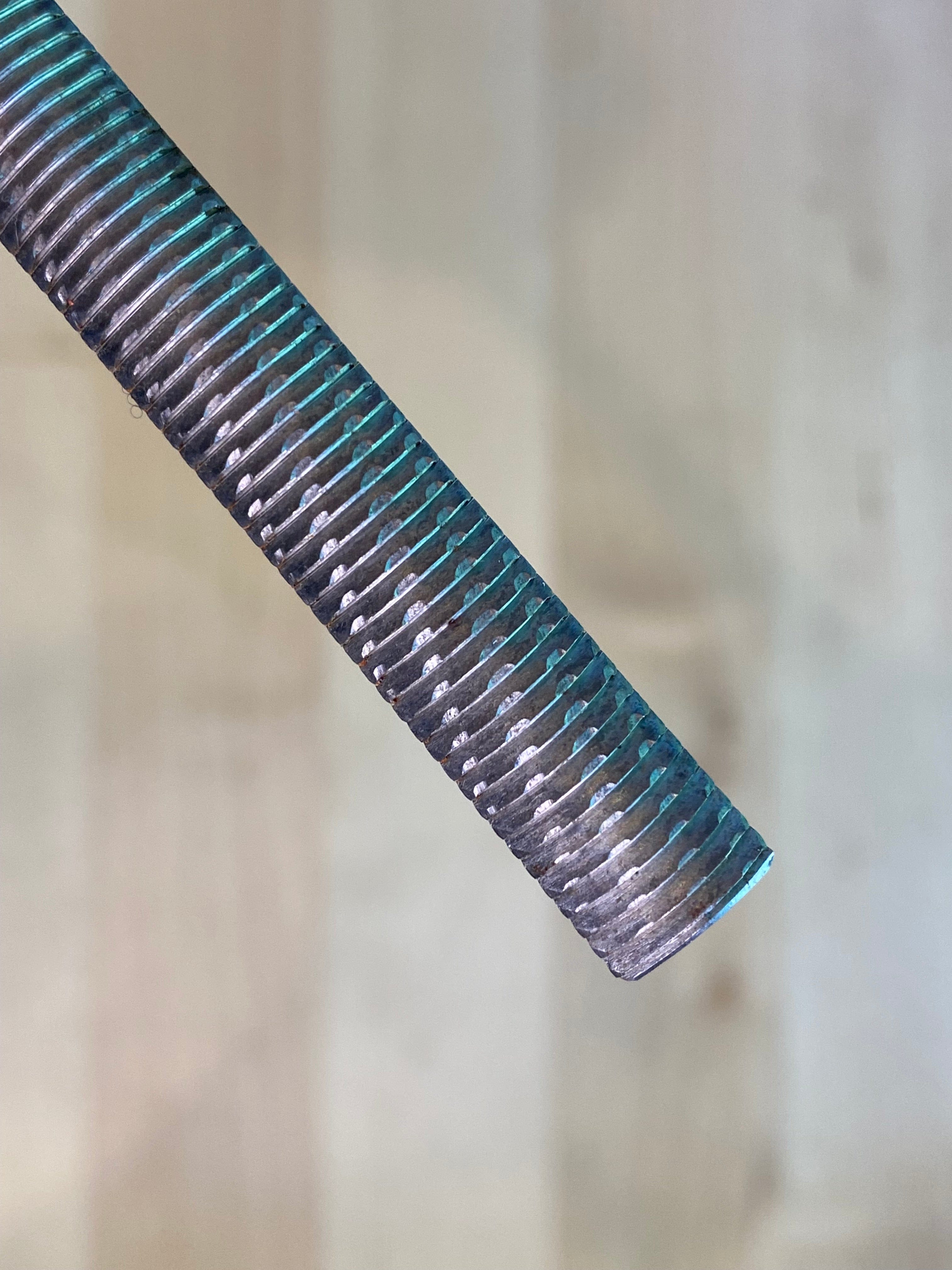 A close-up of a MARU Iwasaki Half Round Ex Fine W/Grip metal rod with horizontal grooves, positioned diagonally against a neutral background, highlights its role as a precision tool in a woodworker's toolkit.