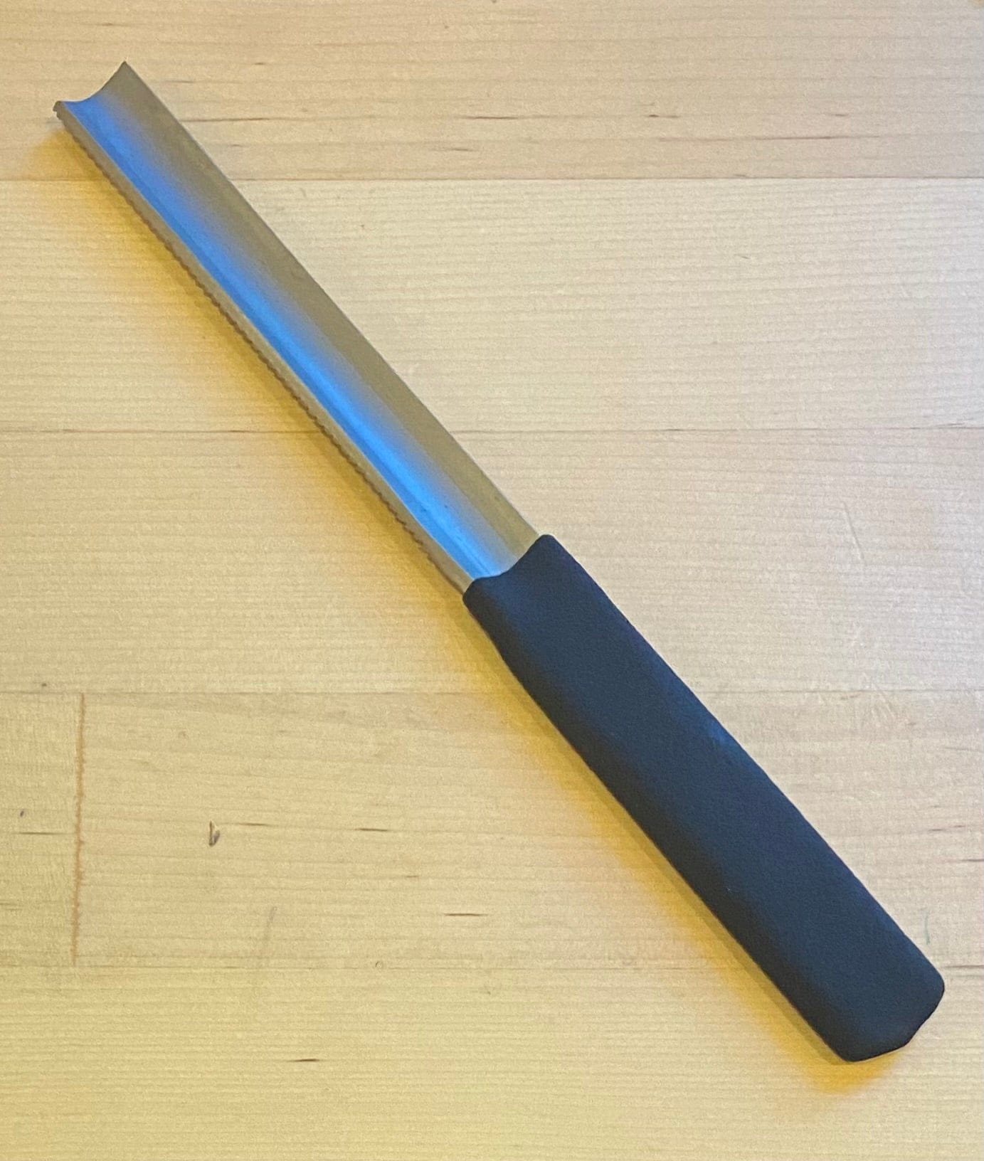 The MARU Half Round Med W/Grip 150mm Wood File, a metal tool with a curved blade and black grip handle, rests on a light wooden surface.