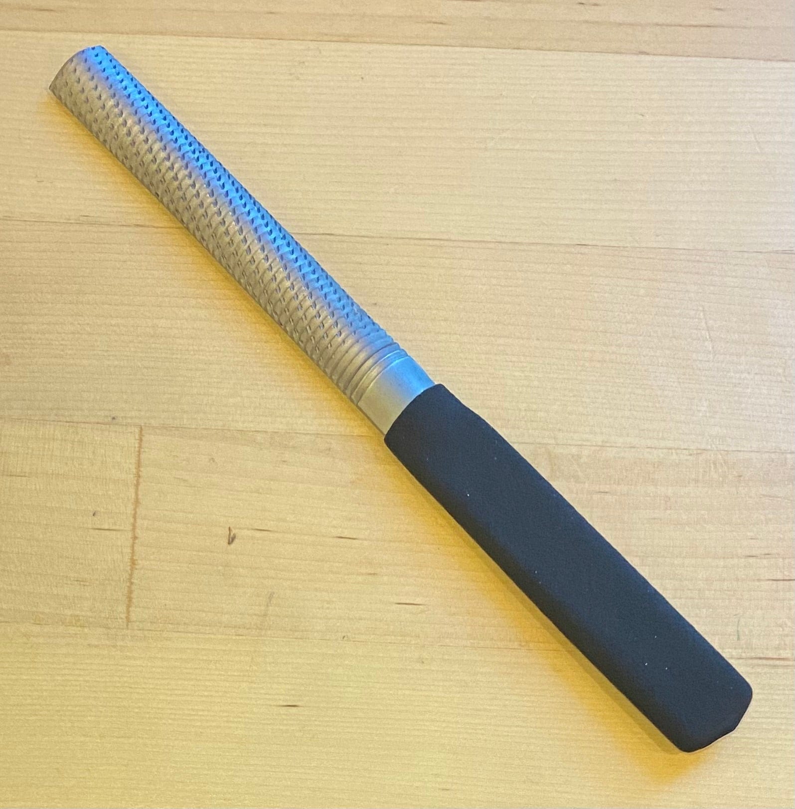 A MARU Half Round Med W/Grip 150mm Wood File with a black handle is resting on a light wooden surface.