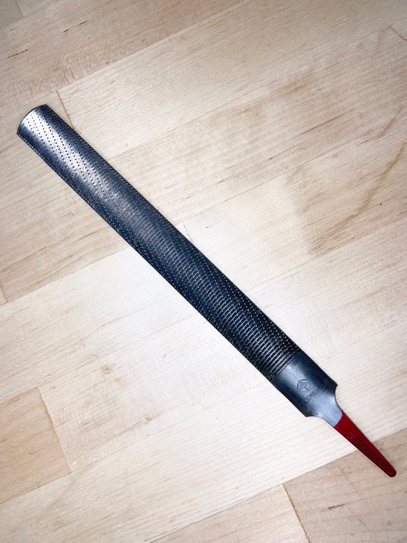 The MARU Iwasaki Half Round Fine Cut Wood File, featuring a 200mm chemically polished, textured metal surface and a red-tipped handle, is placed diagonally on a light wooden surface.