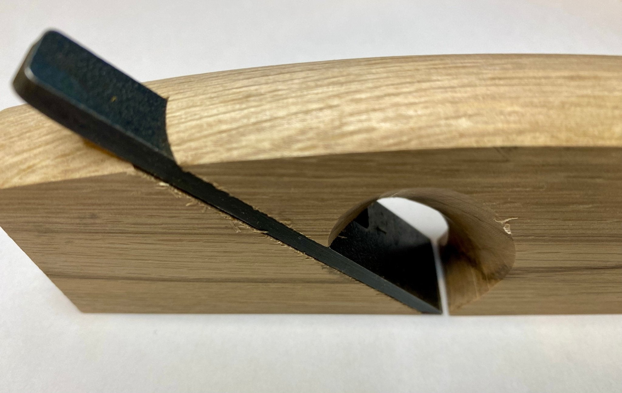 A close-up of the MARU Japanese Rabbet Plane-White Oak, with a high carbon steel blade set at an angle, designed for smoothing and shaping wood surfaces.