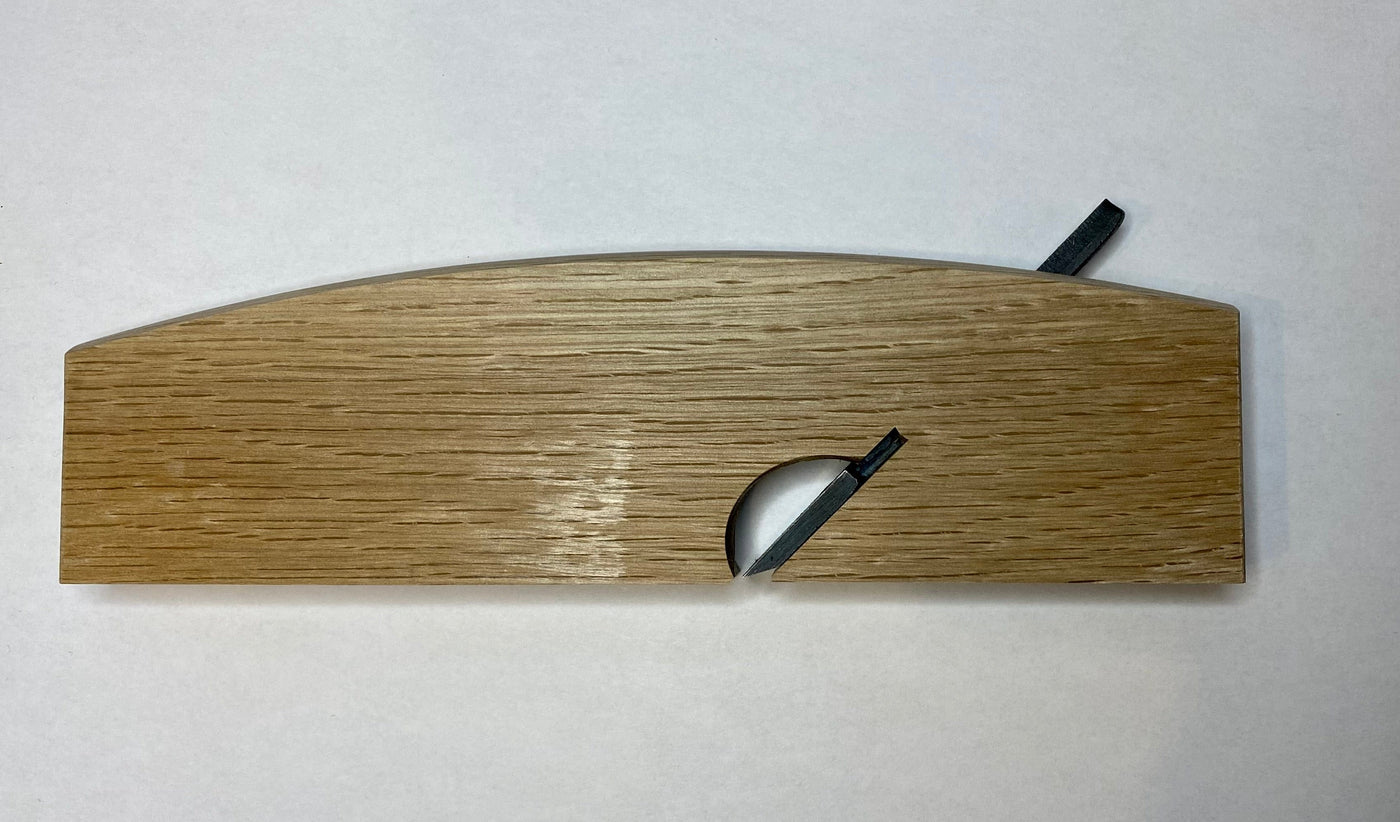 The maru Japanese Rabbet Plane-White Oak is a beautifully crafted woodworking tool, featuring a curved top and a small circular cutout with a protruding black tab, paying homage to traditional Japanese design aesthetics and functionality.