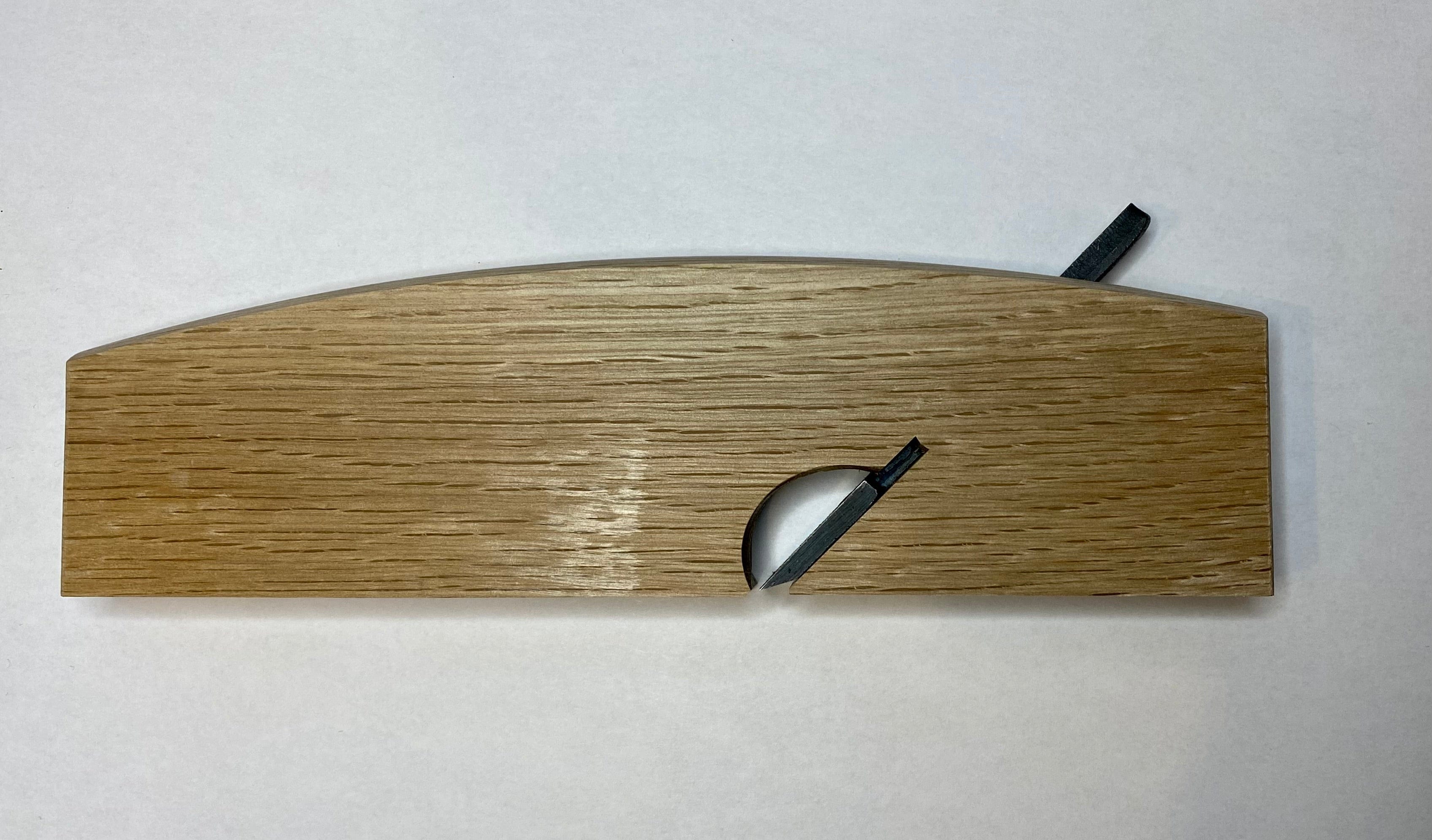 The maru Japanese Rabbet Plane-White Oak is a beautifully crafted woodworking tool, featuring a curved top and a small circular cutout with a protruding black tab, paying homage to traditional Japanese design aesthetics and functionality.