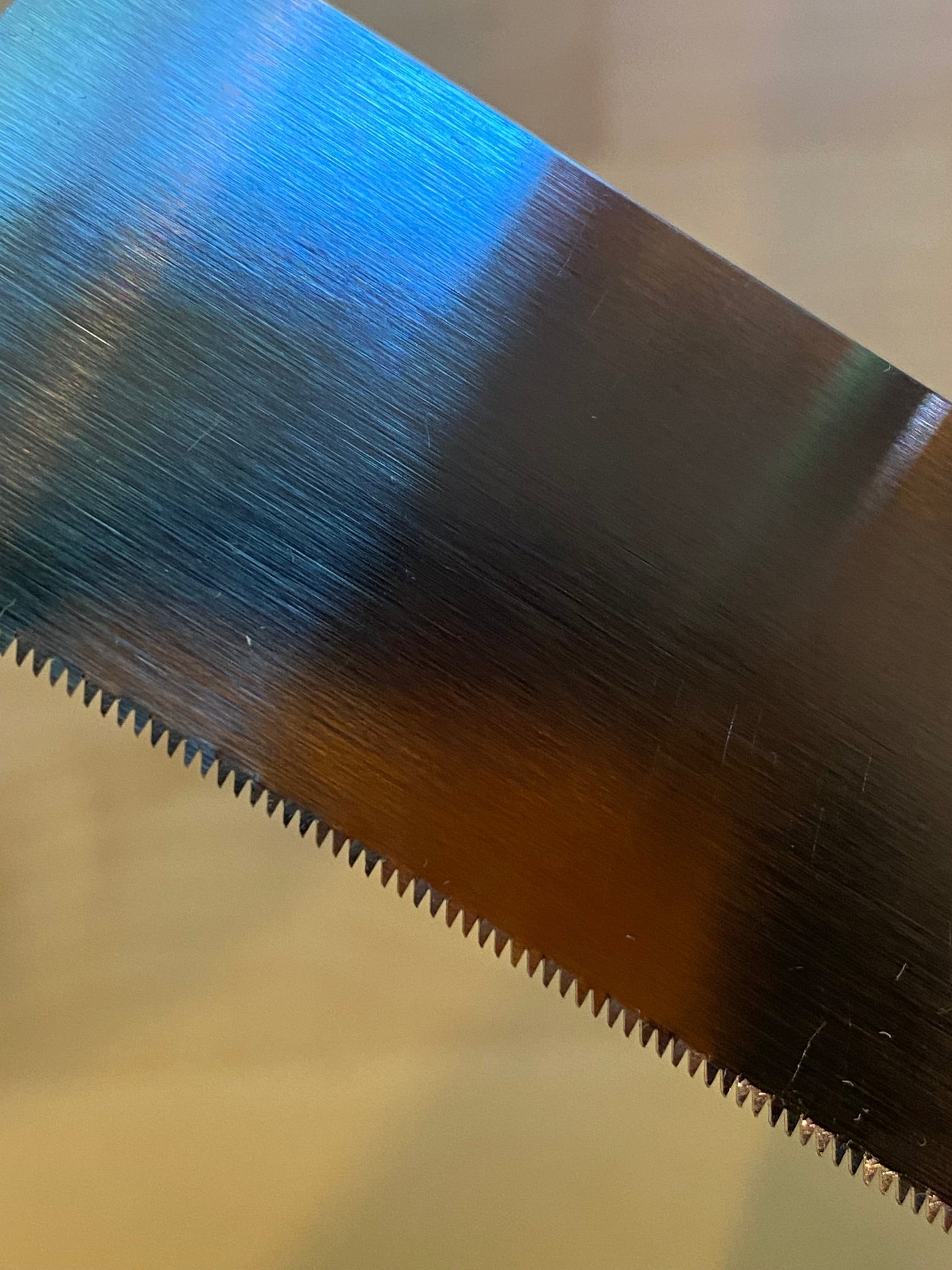 Close-up image of a MARU Small Sheathed Japanese Hand Saw featuring an impulse-hardened serrated blade with light reflections highlighting its precision, ideal for fine woodworking.