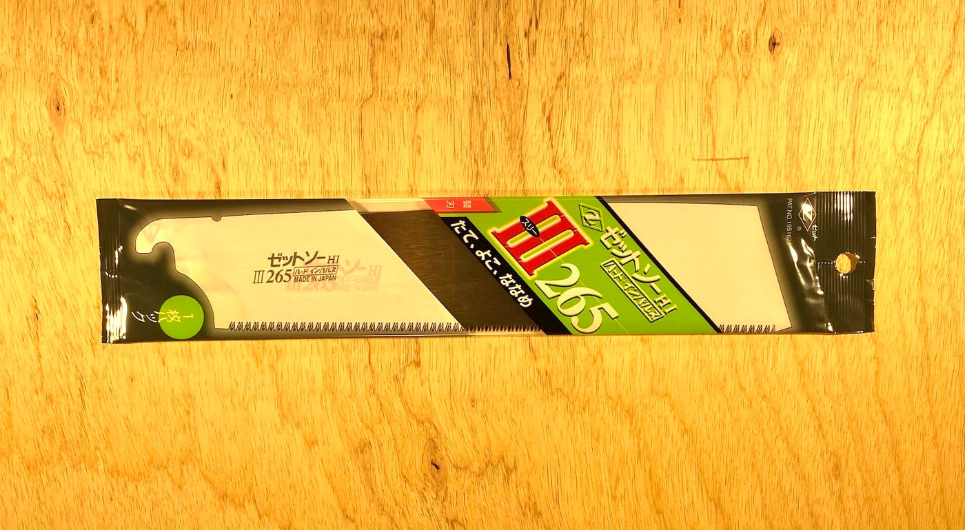 The Z-Saw Universal Saw 265 by MARU features chisel-like teeth and a black handle. Its packaged with a green and red label, resting on a wooden surface.