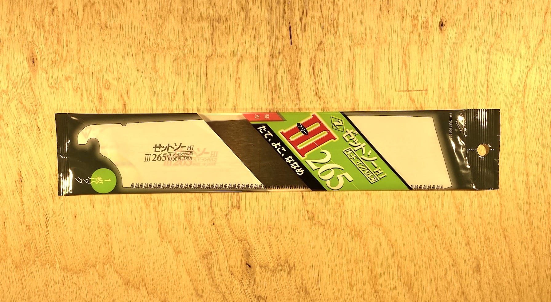 The Z-Saw Universal Saw 265 by MARU features chisel-like teeth and a black handle. Its packaged with a green and red label, resting on a wooden surface.