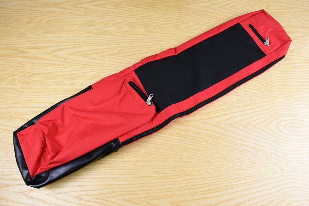 A Hand Saw Bag from MARU, featuring a red and black padded design with zippers and pockets for storage, lies on a light wood surface—perfect for woodworking enthusiasts.