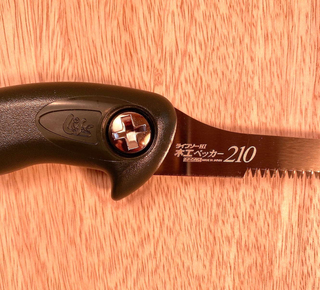 Close-up of a Key Hole Saw by Z-Saw in fashion with a black handle and a 210mm serrated, impulse hardened blade, placed on a wooden surface. The handle features the name "MARU" and the blade is labeled "Made in Japan 210".