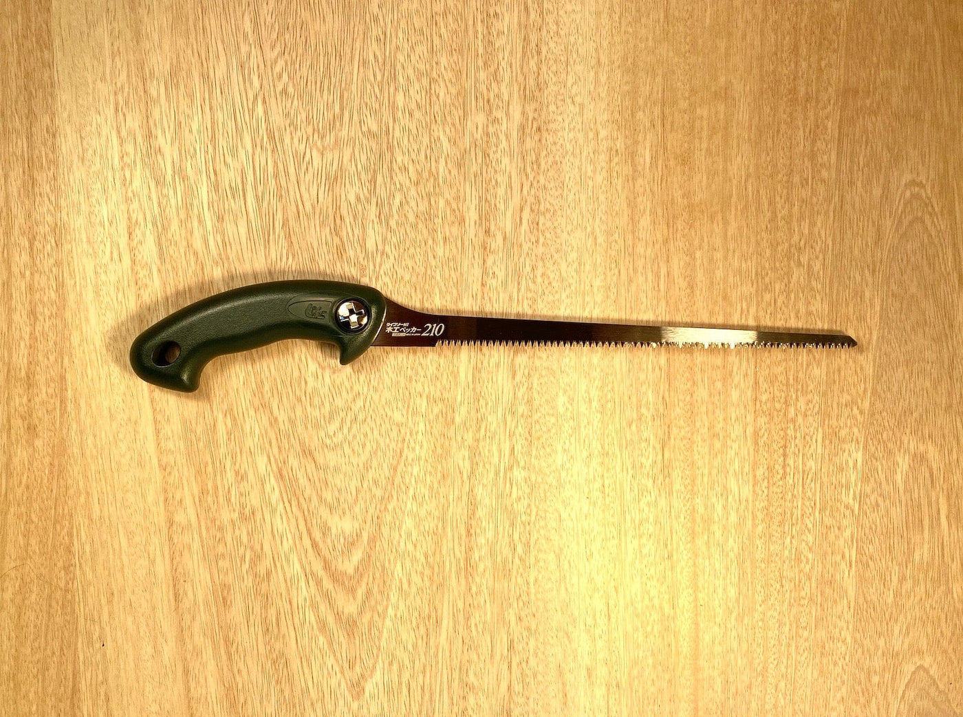 The Key Hole Saw by Z-Saw, crafted by MARU and featuring a black ergonomic handle and a long, impulse-hardened serrated blade designed in Japanese-Pull-Saw-Fashion, is placed on a wooden surface.