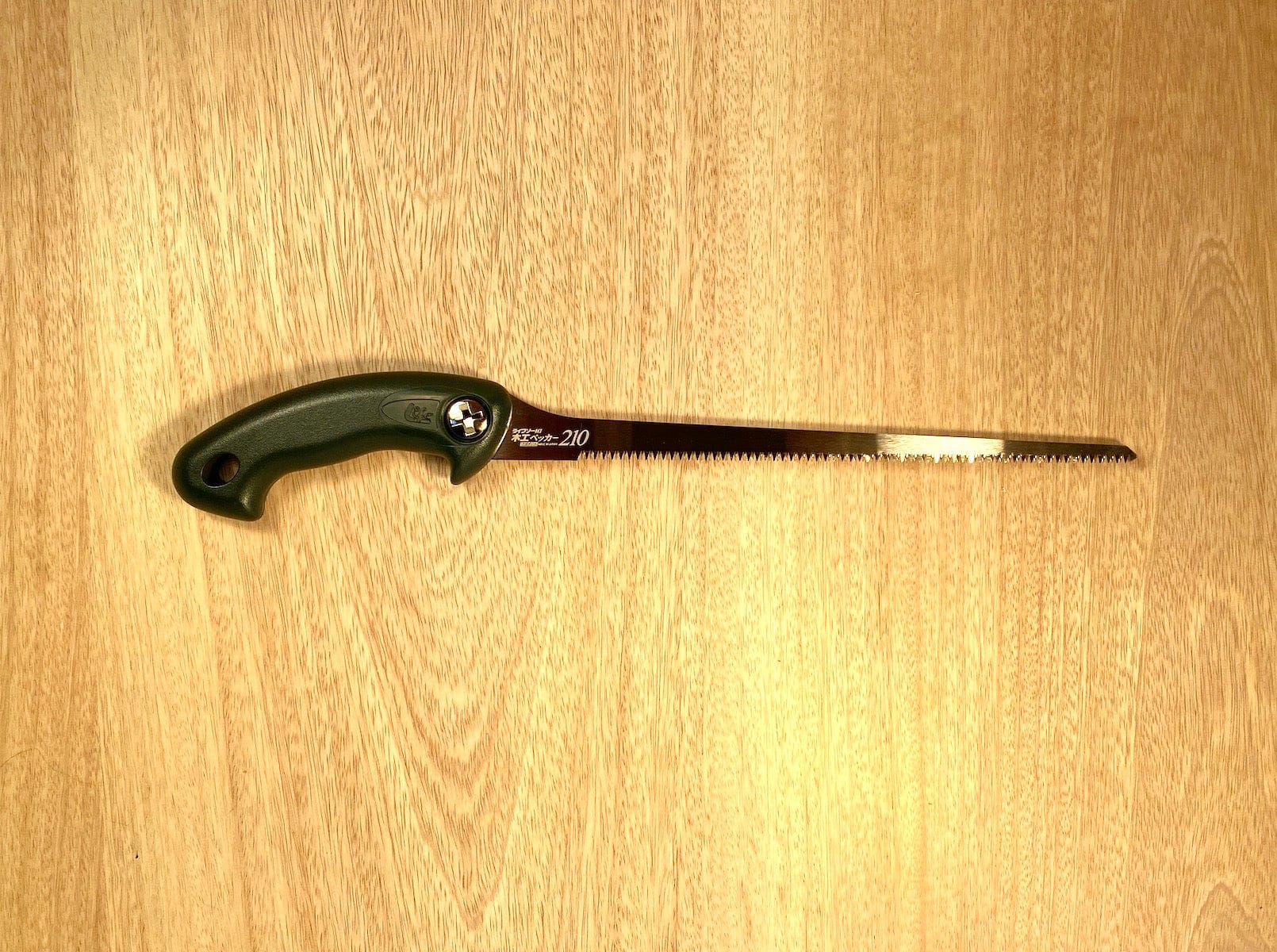 The Key Hole Saw by Z-Saw, crafted by MARU and featuring a black ergonomic handle and a long, impulse-hardened serrated blade designed in Japanese-Pull-Saw-Fashion, is placed on a wooden surface.