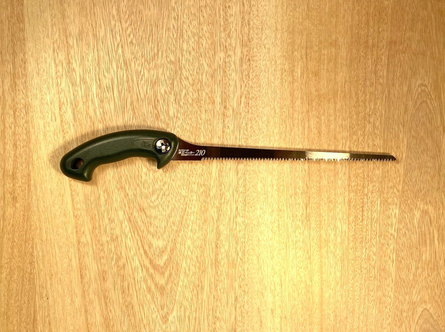 The Key Hole Saw by Z-Saw, crafted by MARU and featuring a black ergonomic handle and a long, impulse-hardened serrated blade designed in Japanese-Pull-Saw-Fashion, is placed on a wooden surface.