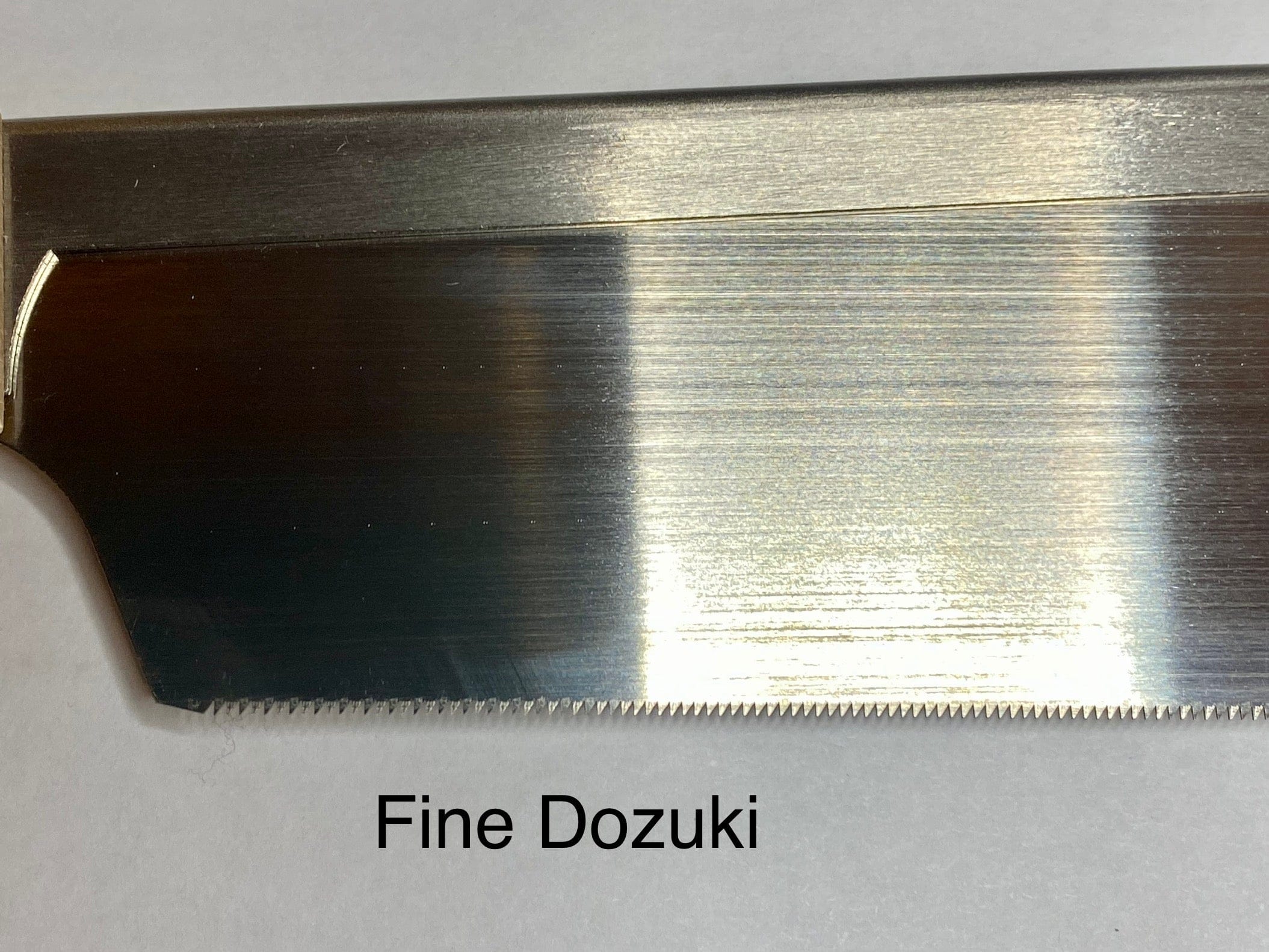 Close-up of a MARU Japanese Craft Saw blade, showcasing precision akin to a ryoba. Its sharp, finely spaced teeth are set against a plain white background, emphasizing craftsmanship and the ergonomic grip of its beech wood handle.