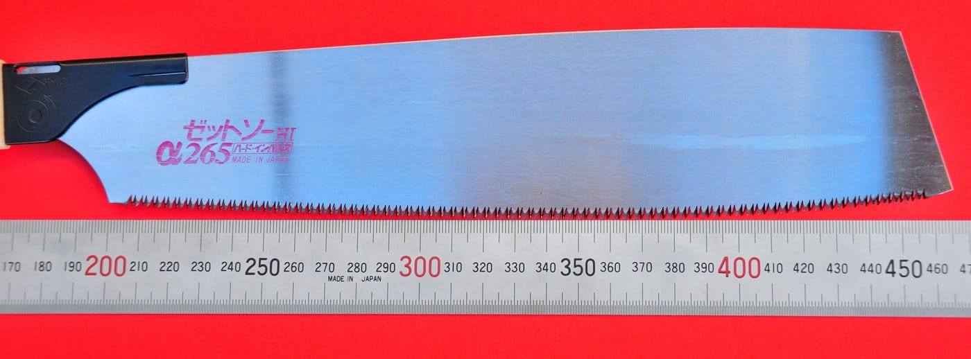 A Curved-Edge Z-Saw 265 by MARU with a 265mm blade and impulse-hardened teeth sits alongside a steel ruler, all set against a red background.