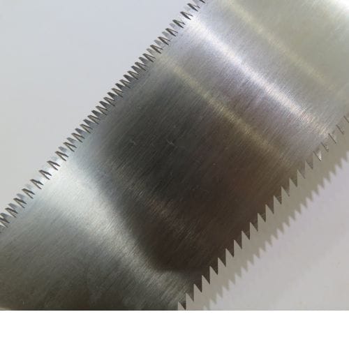 Close-up of a MARU Japanese Craft Saws serrated metal blade featuring dual-sized teeth against a neutral backdrop, showcasing the precision of its design with a smooth beech wood handle.