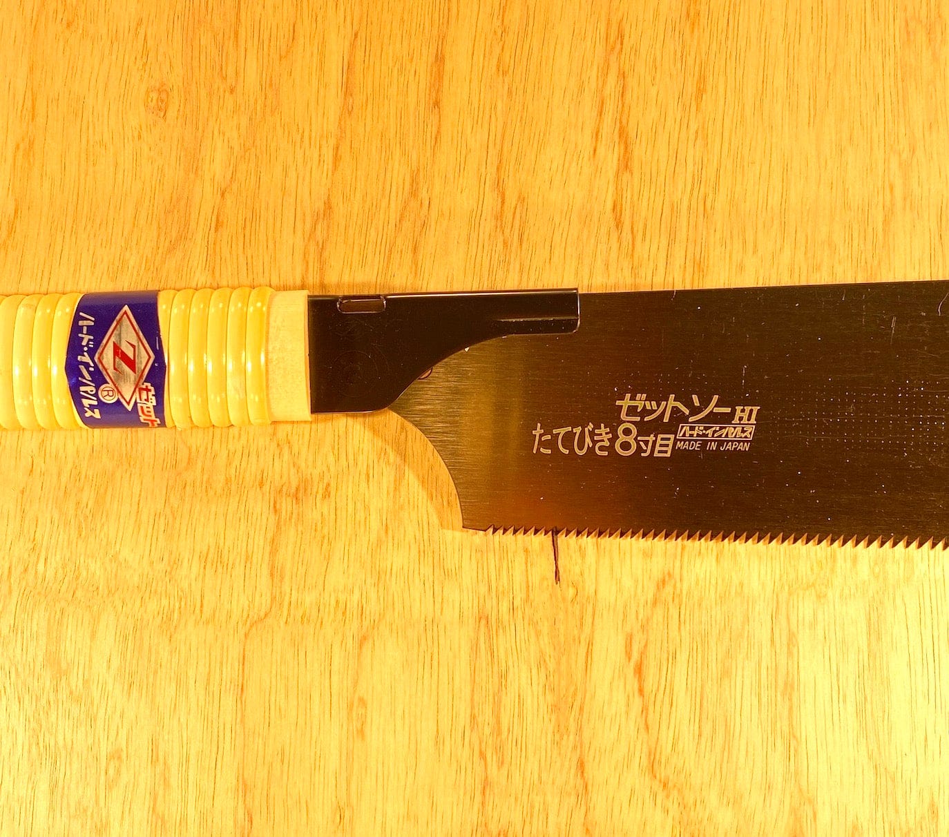 The Rip H-250 by Z-Saw from MARU features a yellow handle and rip-tooth blade, resting on wood. Japanese characters and Made in Japan appear on the blade, highlighting this saw’s precision craftsmanship.