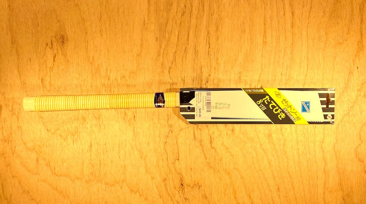 The Rip H-250 by Z-Saw from MARU, featuring a yellow grip and a black-and-yellow label inspired by rip saw teeth, rests flat on a light wooden surface.