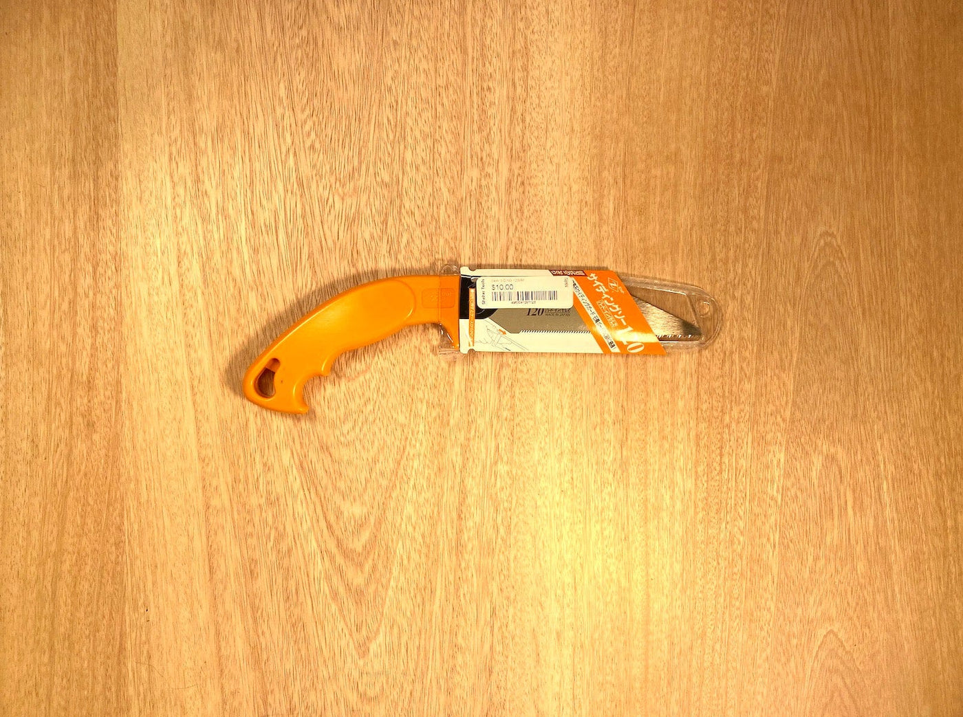 A compact saw with an orange handle from the MARU brand, called the Siding Saw by Z-Saw, rests on a wooden surface with its partially open blade ready to cut siding or plaster board.