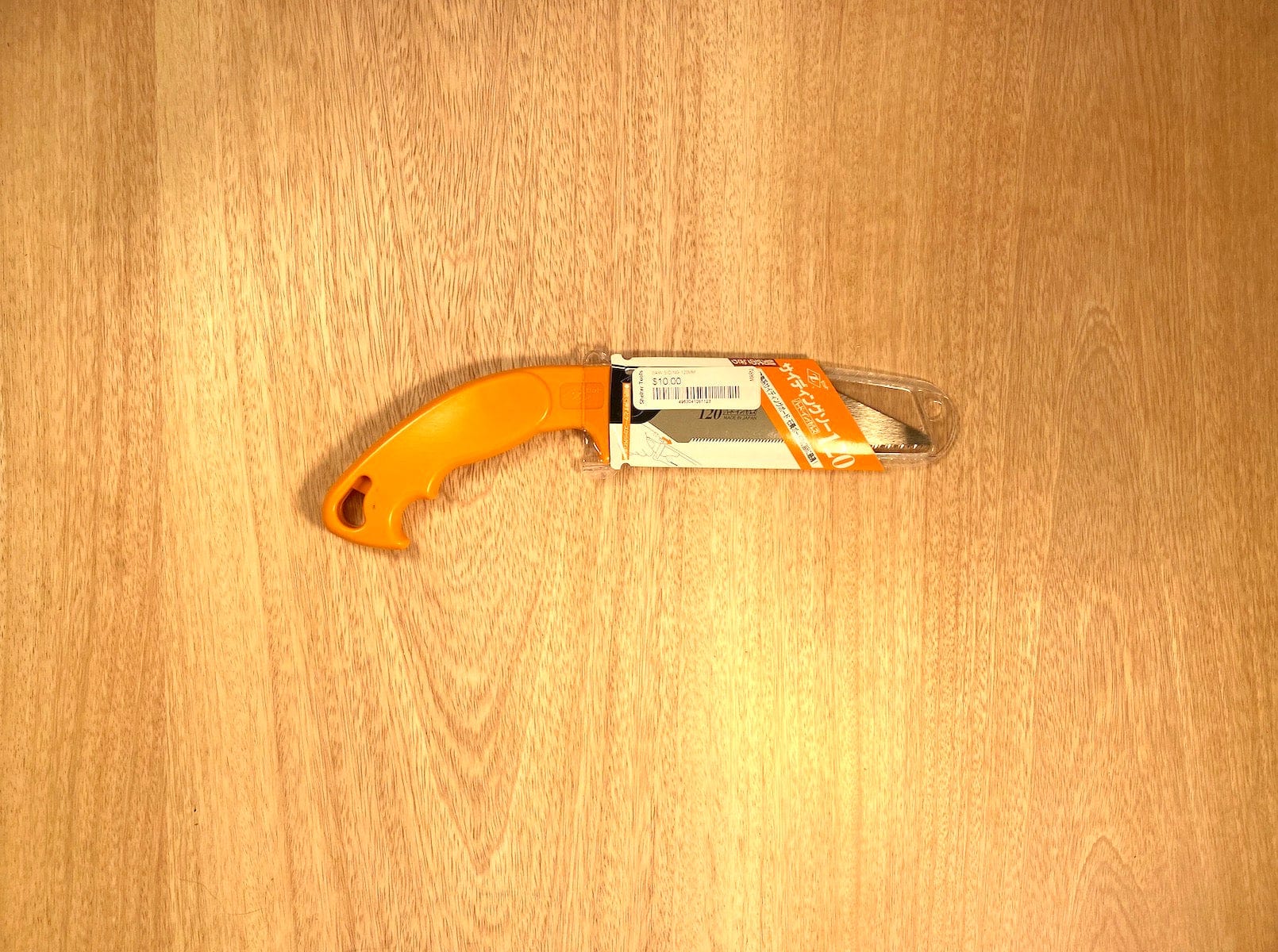 A compact saw with an orange handle from the MARU brand, called the Siding Saw by Z-Saw, rests on a wooden surface with its partially open blade ready to cut siding or plaster board.